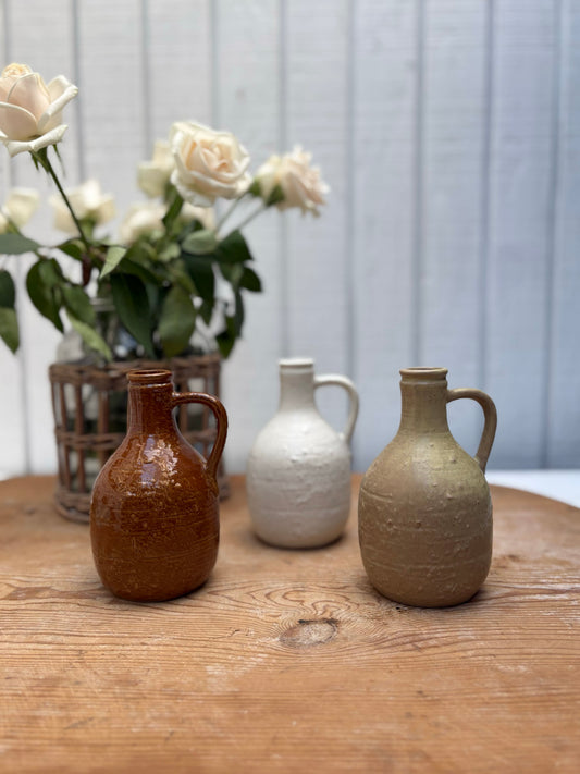 Three ceramic jars on a wooden surface with a blurred background of white flowers.