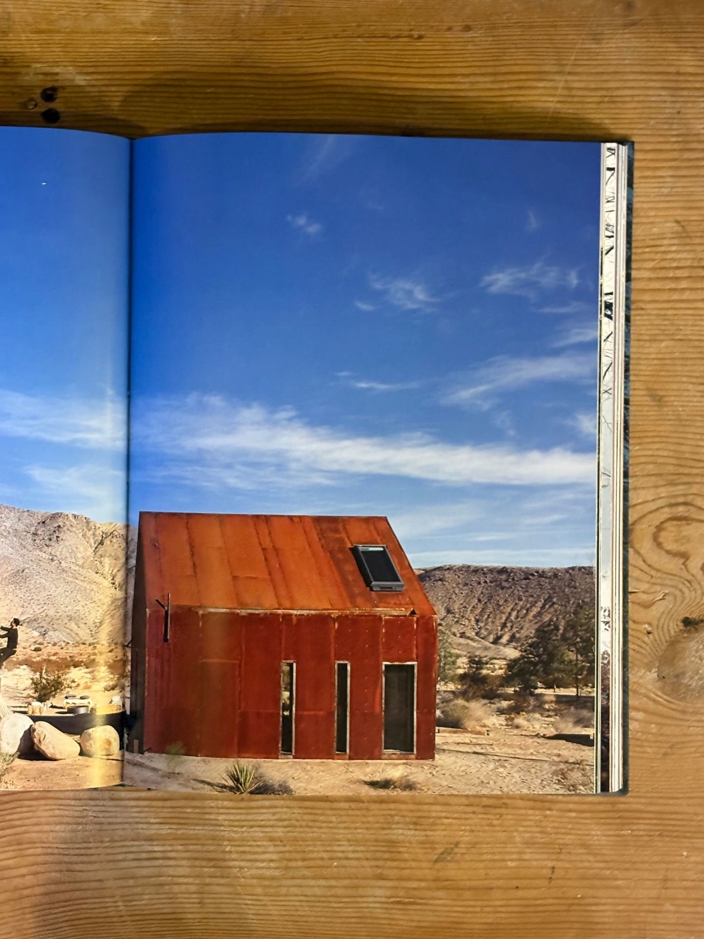 Book open to a page showing a desert landscape with a rusted metal building.