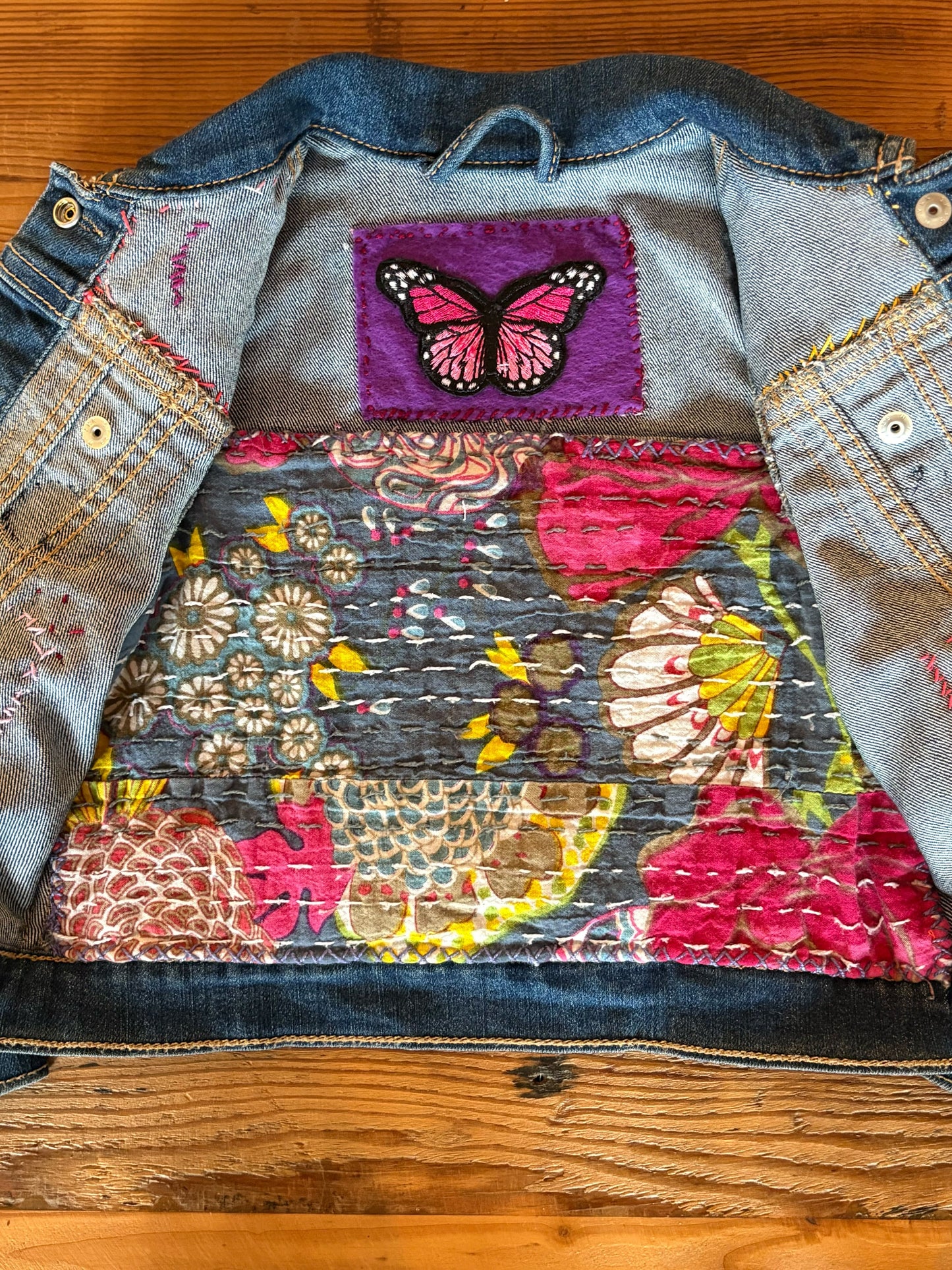Upcycled denim jacket with floral and butterfly design on a wooden surface