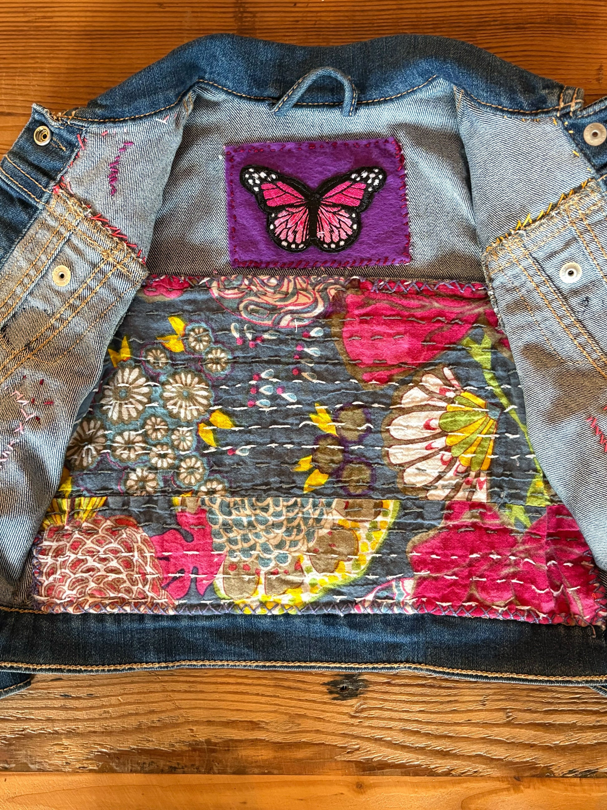 Upcycled denim jacket with floral and butterfly design on a wooden surface
