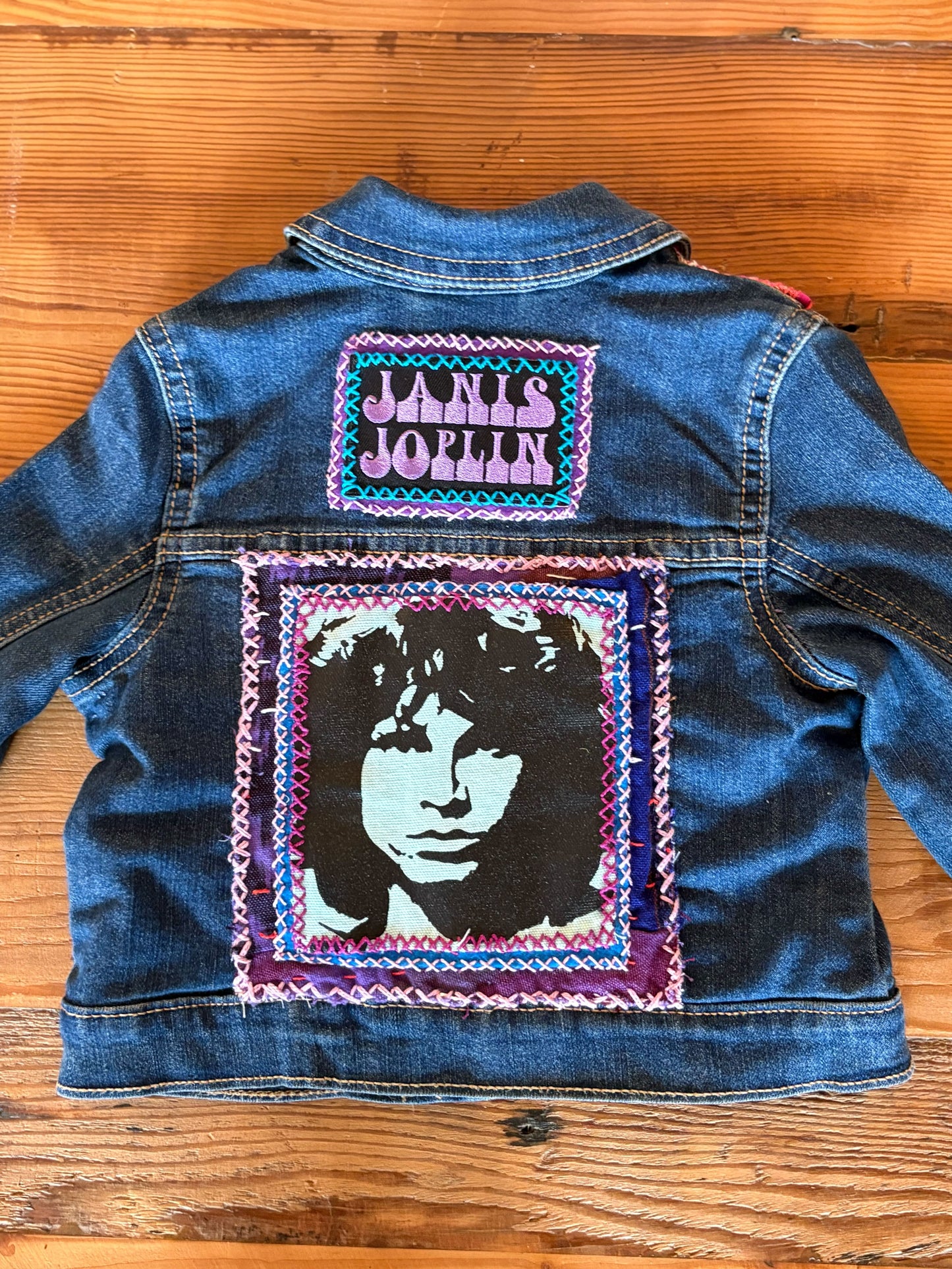Denim jacket with Janis Joplin patch on a wooden surface