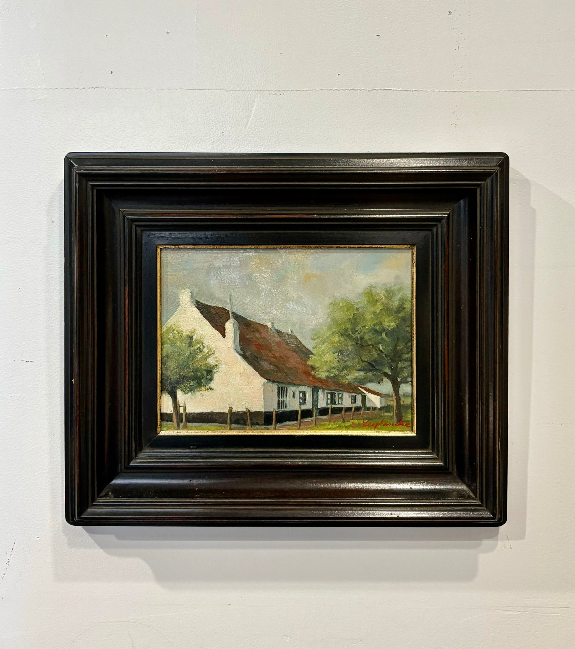 Framed painting of a house with trees on a white wall