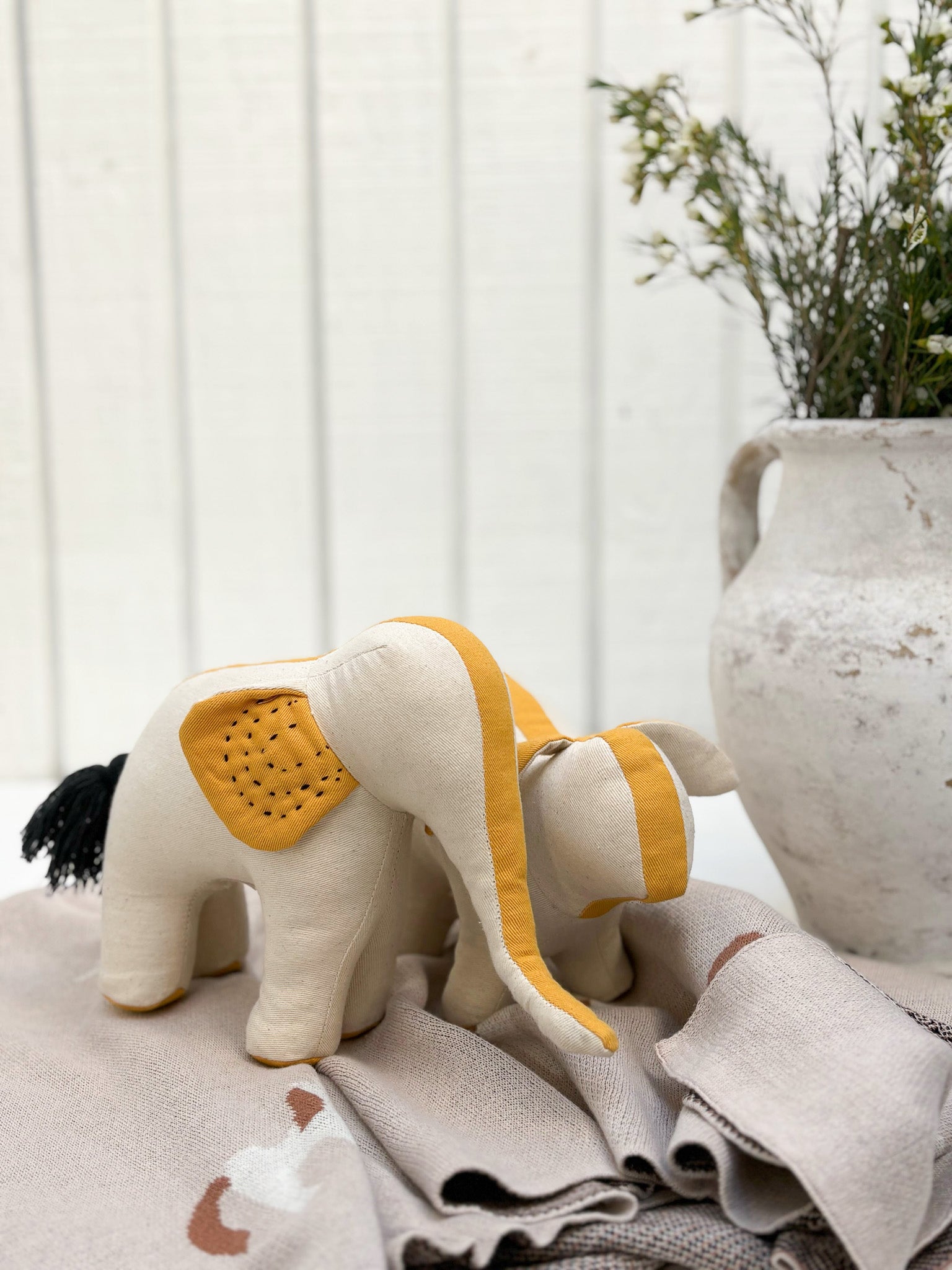 Stuffed elephant toy with yellow accents on a textured surface with a blurred background