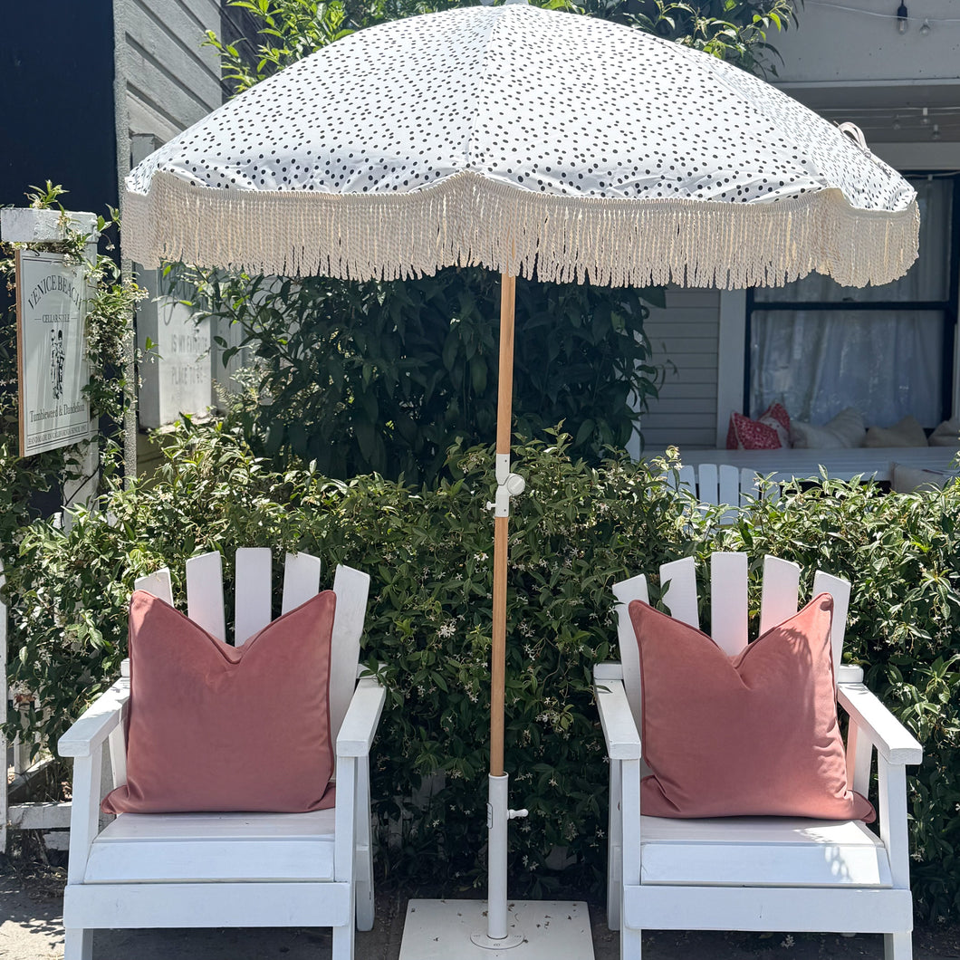 Two white chairs with pink cushions under a polka dot umbrella in a garden setting.