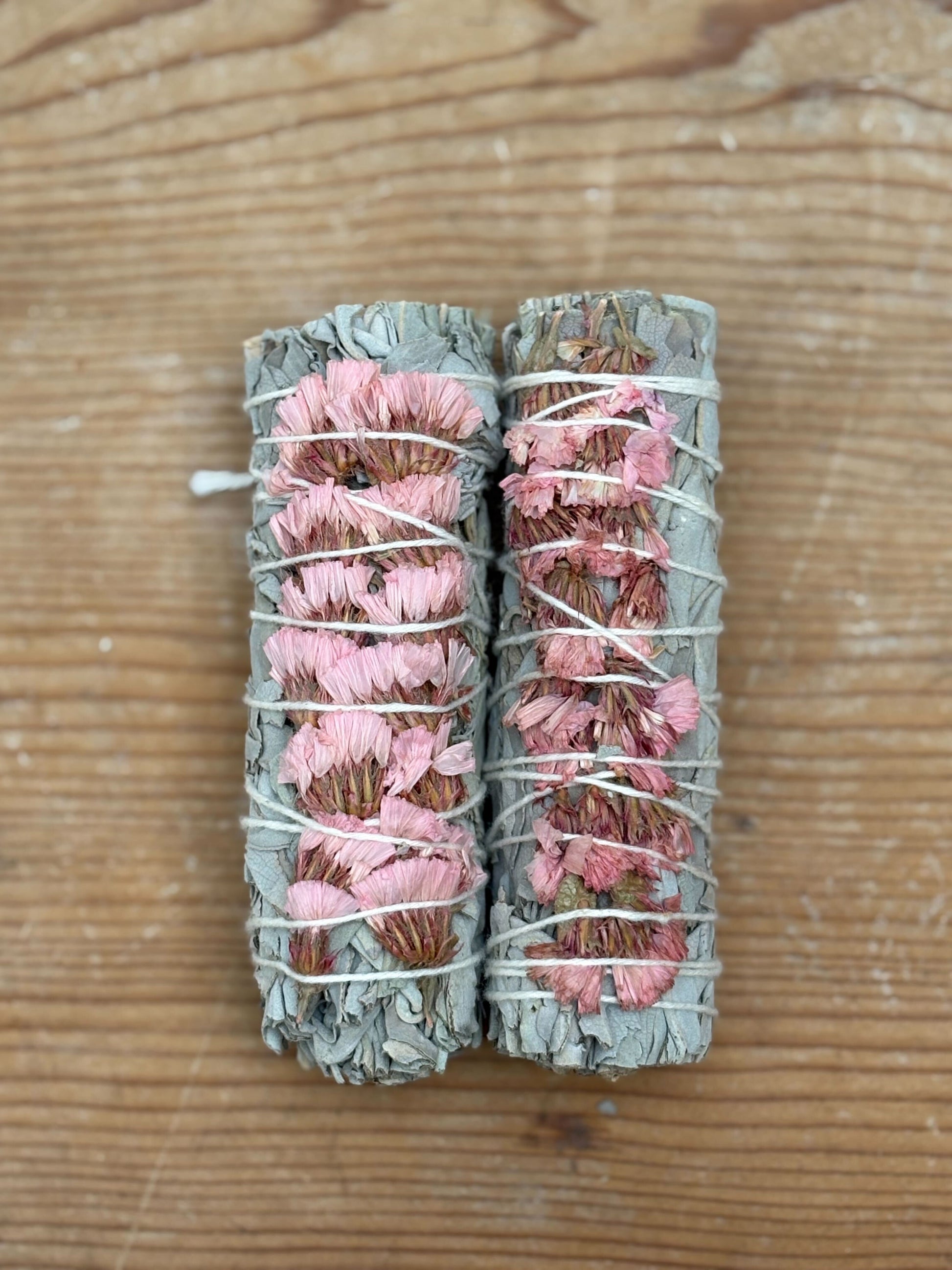 Two bundles of pink and green smudge sticks tied together on a wooden surface.