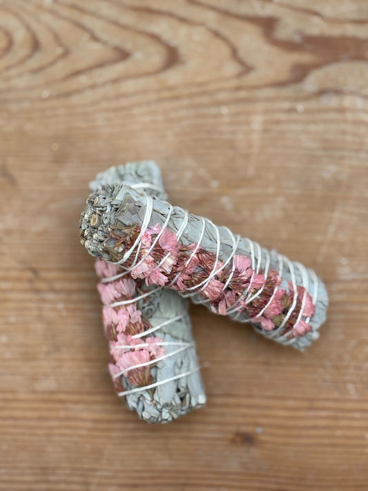 Two bundles of sage wrapped in pink flowers on a wooden surface