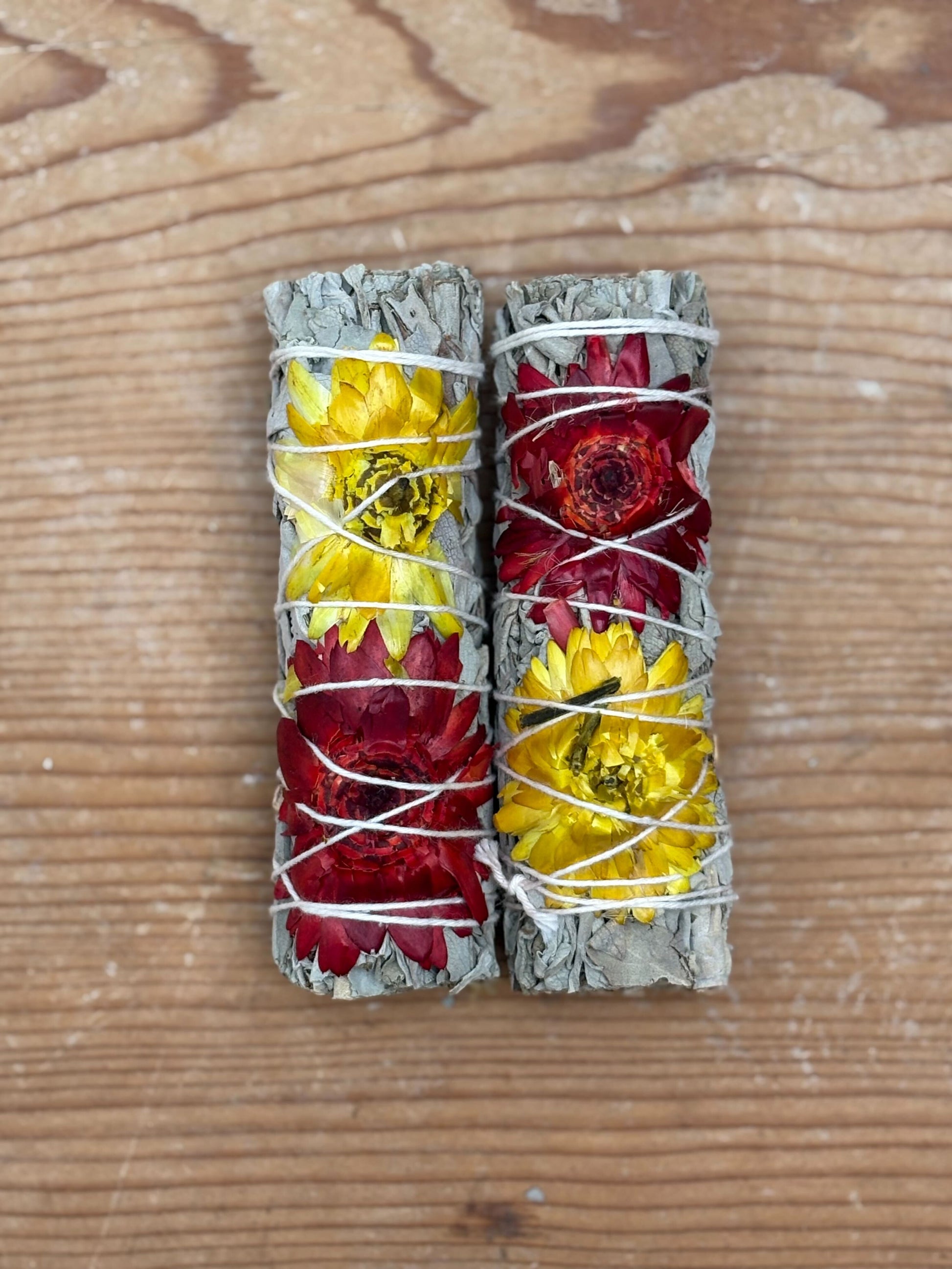 Two bundles of sage with flowers wrapped in twine on a wooden surface