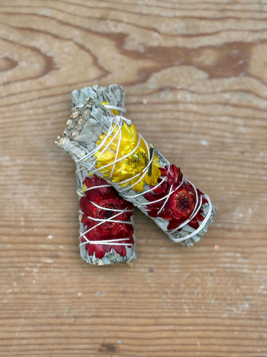 Two smudge sticks wrapped with red and yellow materials on a wooden surface