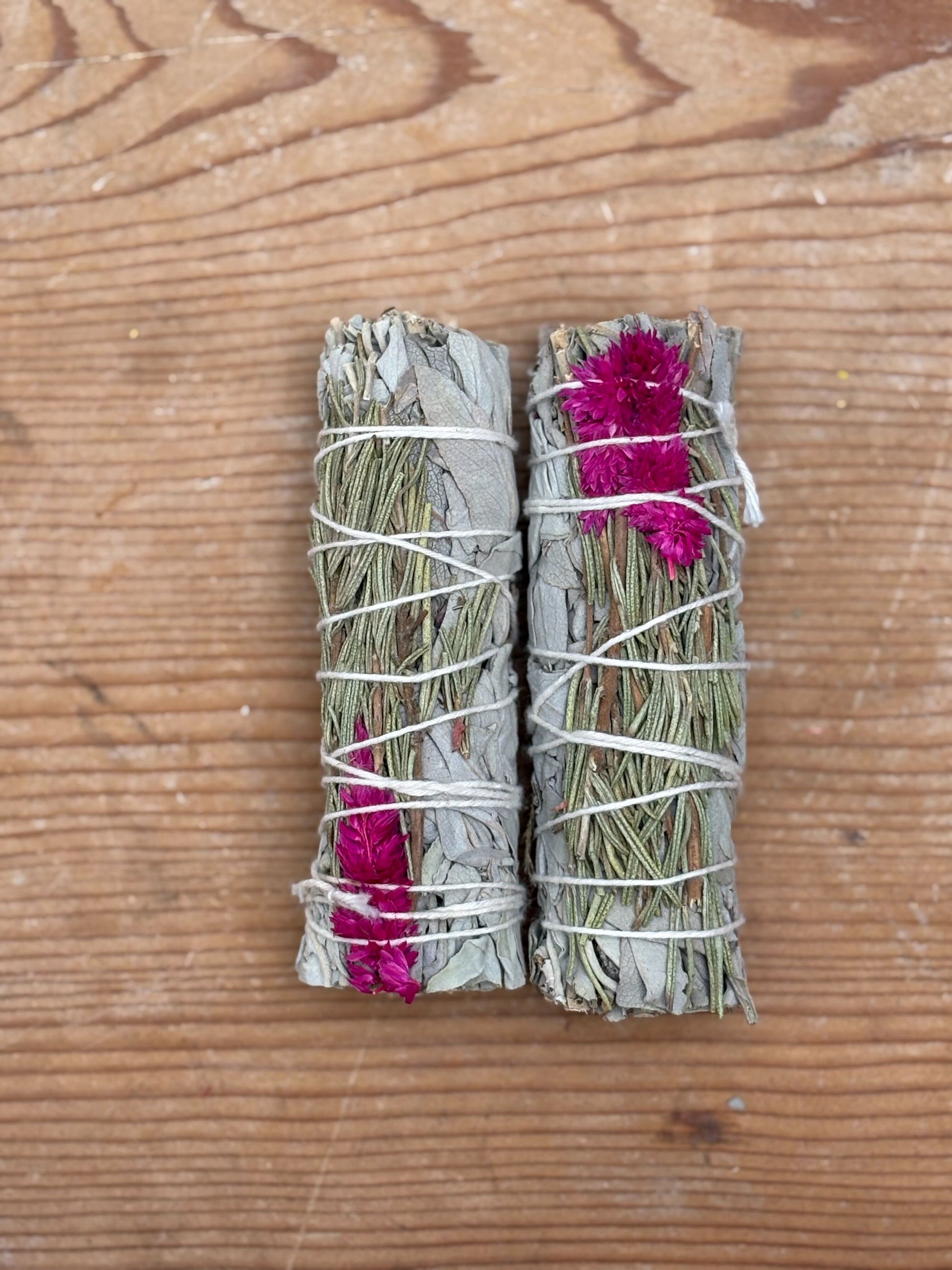 Two bundles of sage and rosemary tied with twine on a wooden surface
