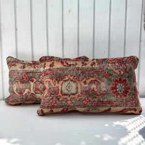 Two patterned pillows on a white surface with a light wooden panel background