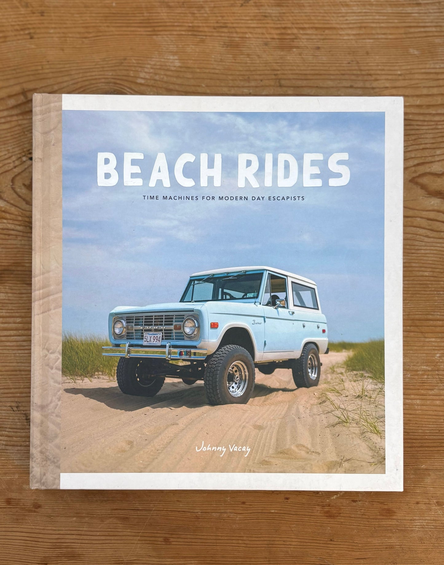 Book titled 'Beach Rides' with a vintage SUV on a beach cover, placed on a wooden surface.