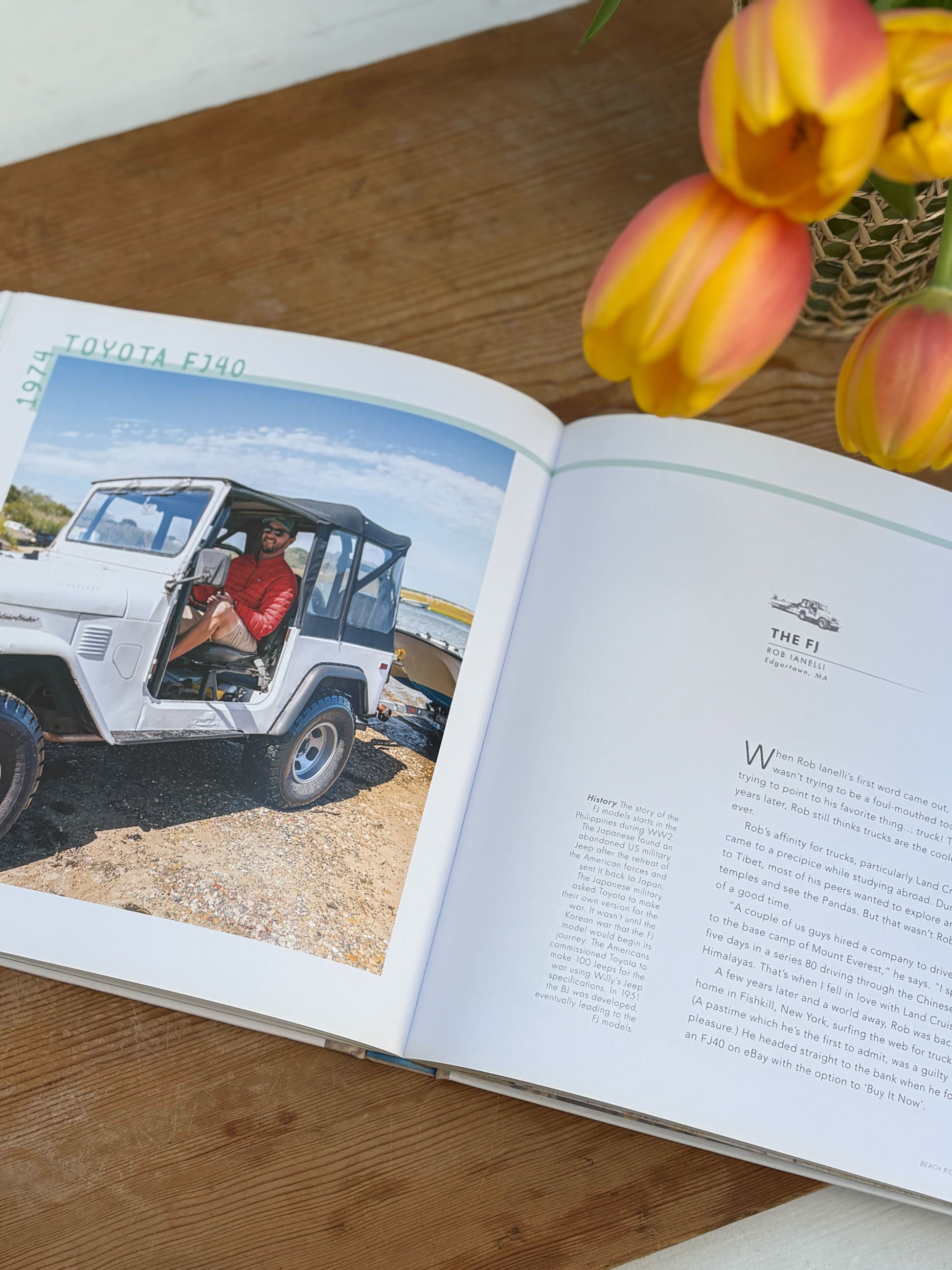Open book on a wooden surface with a Toyota FJ40 vehicle image and yellow tulips.