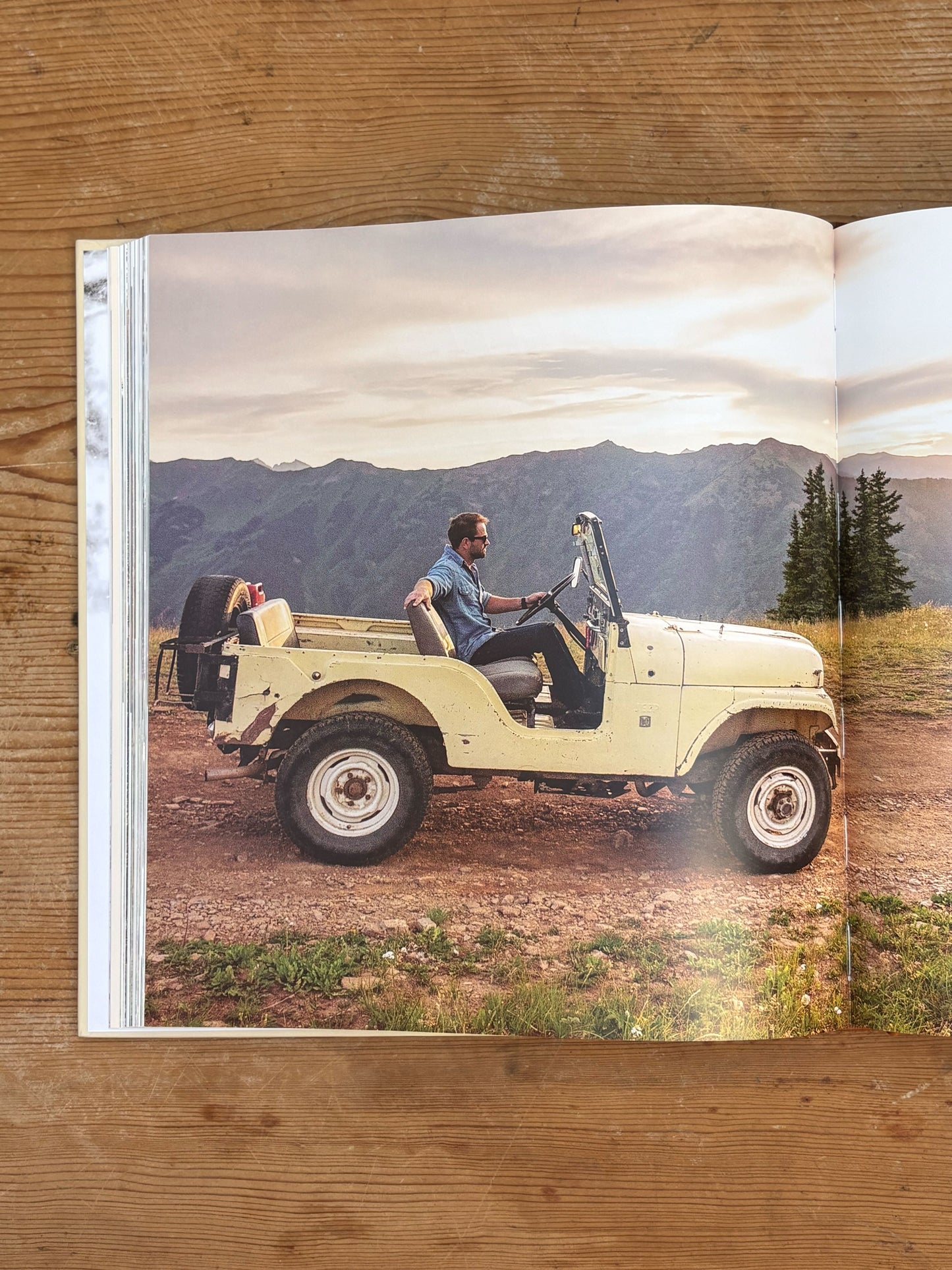 Open book showing a photo of two people in an old-fashioned jeep with mountains in the background