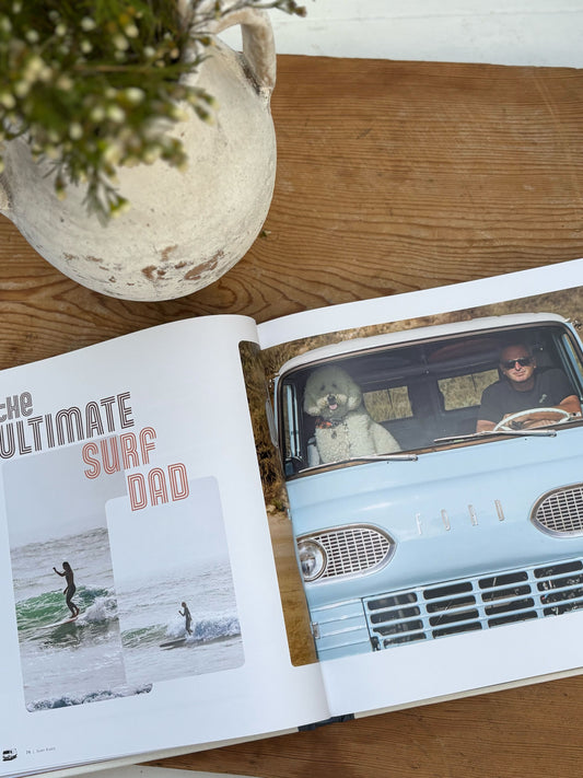 Open book on a wooden surface with a photo of a man driving a vintage car and text 'The Ultimate Surf Dad'.
