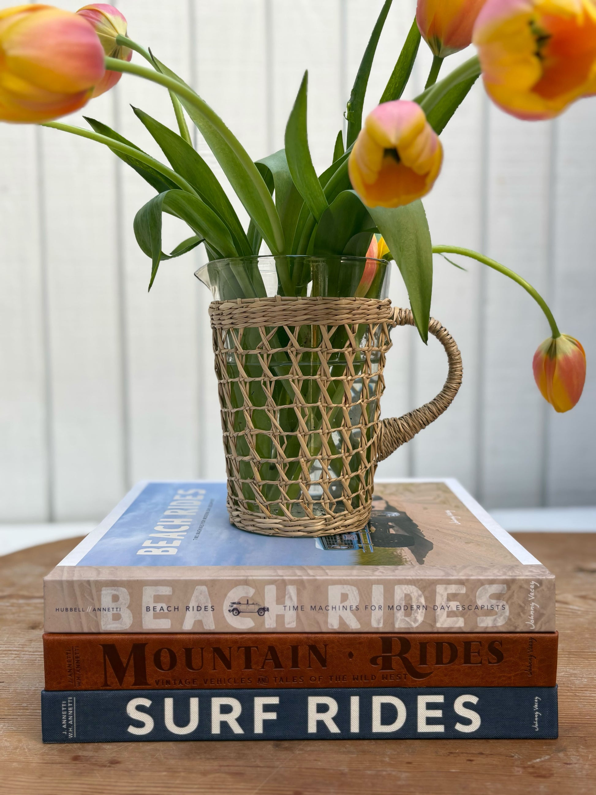 Vase with flowers on top of books titled 'Beach Rides', 'Mountain Rides', and 'Surf Rides' on a wooden surface.