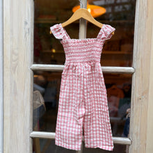 Load image into Gallery viewer, Pink checkered jumpsuit hanging on a wooden hanger against a glass door.