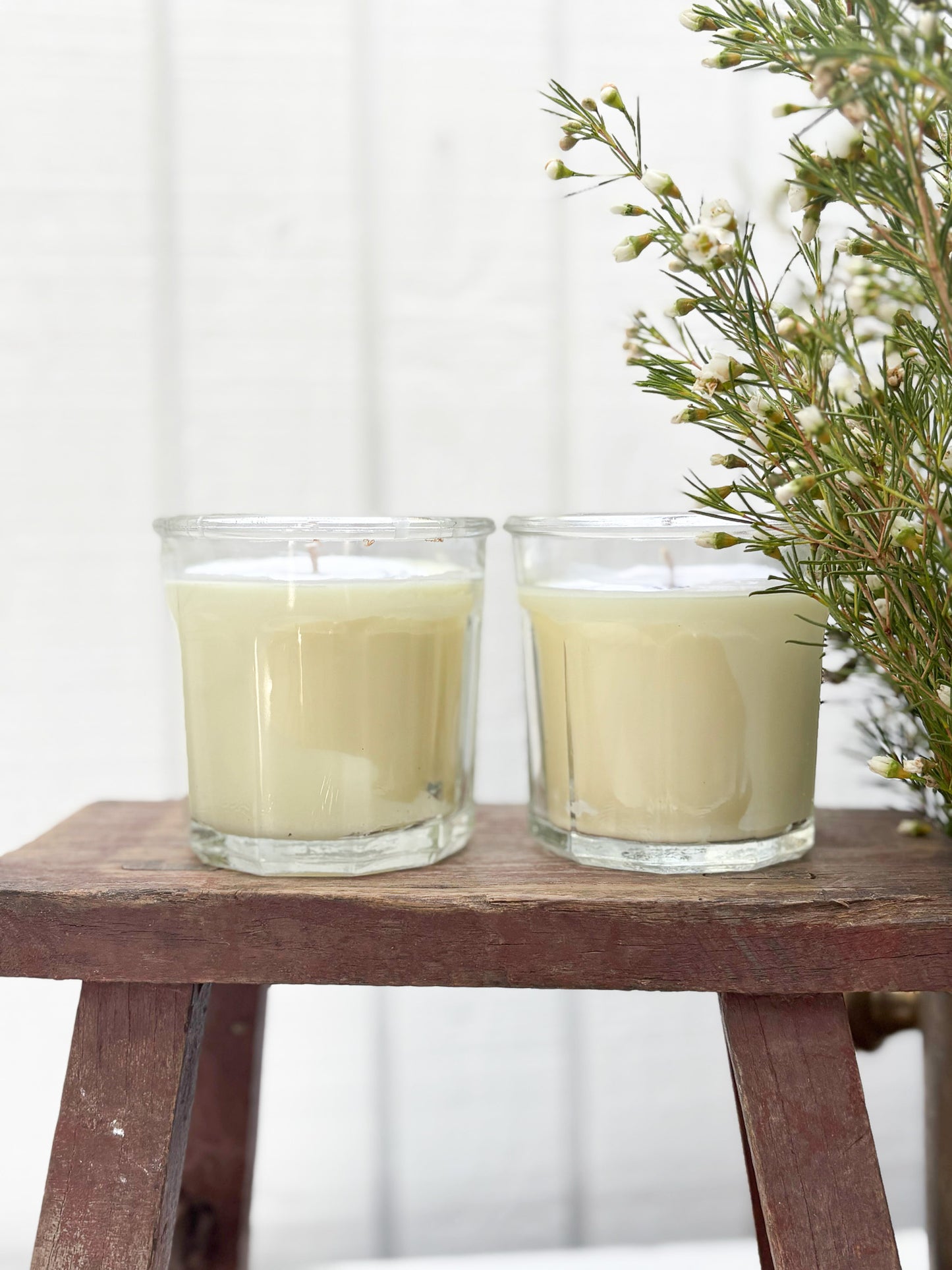 Two glass candles on a wooden stool with a white background