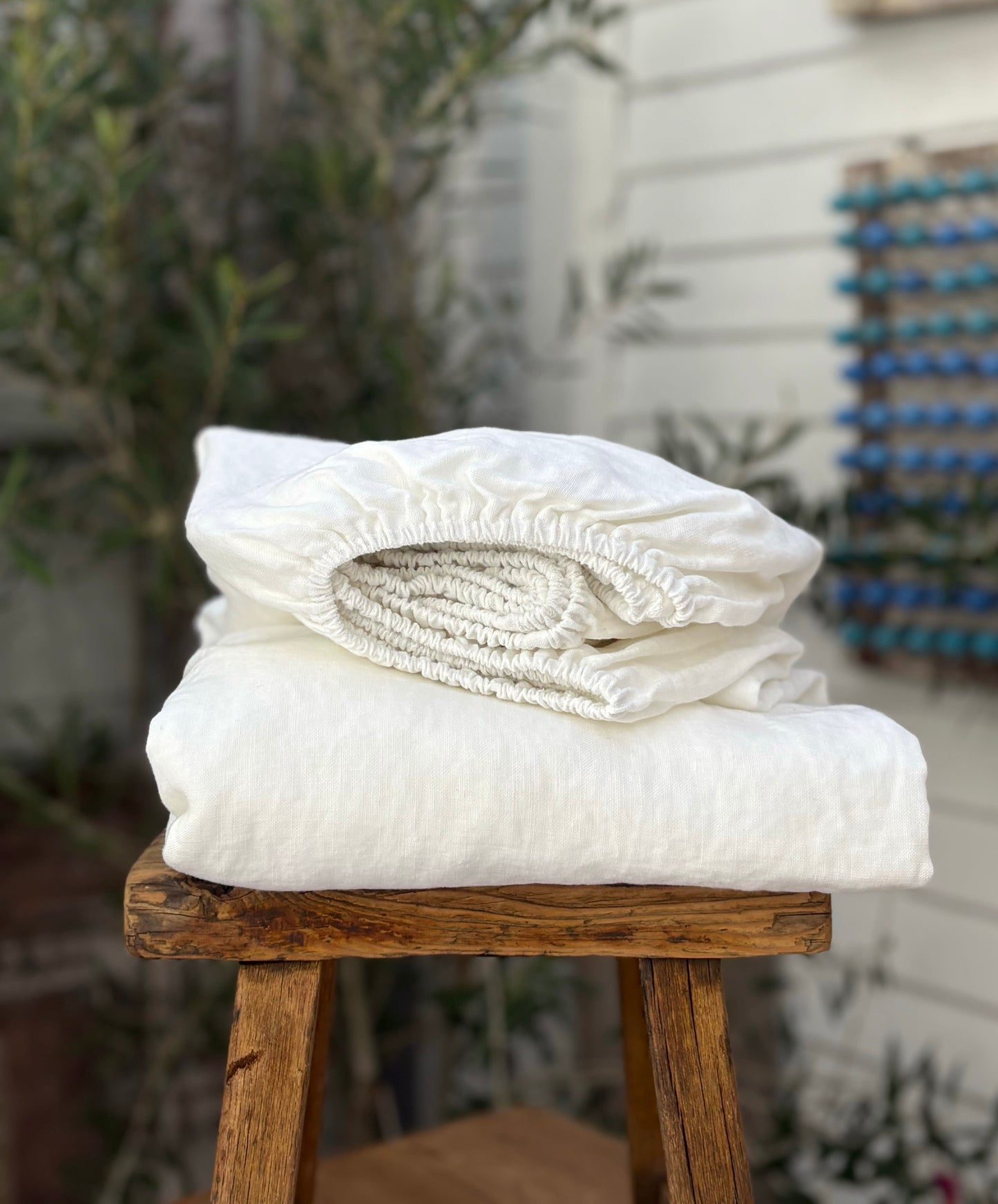 Folded white bedding on a wooden stool with a blurred background