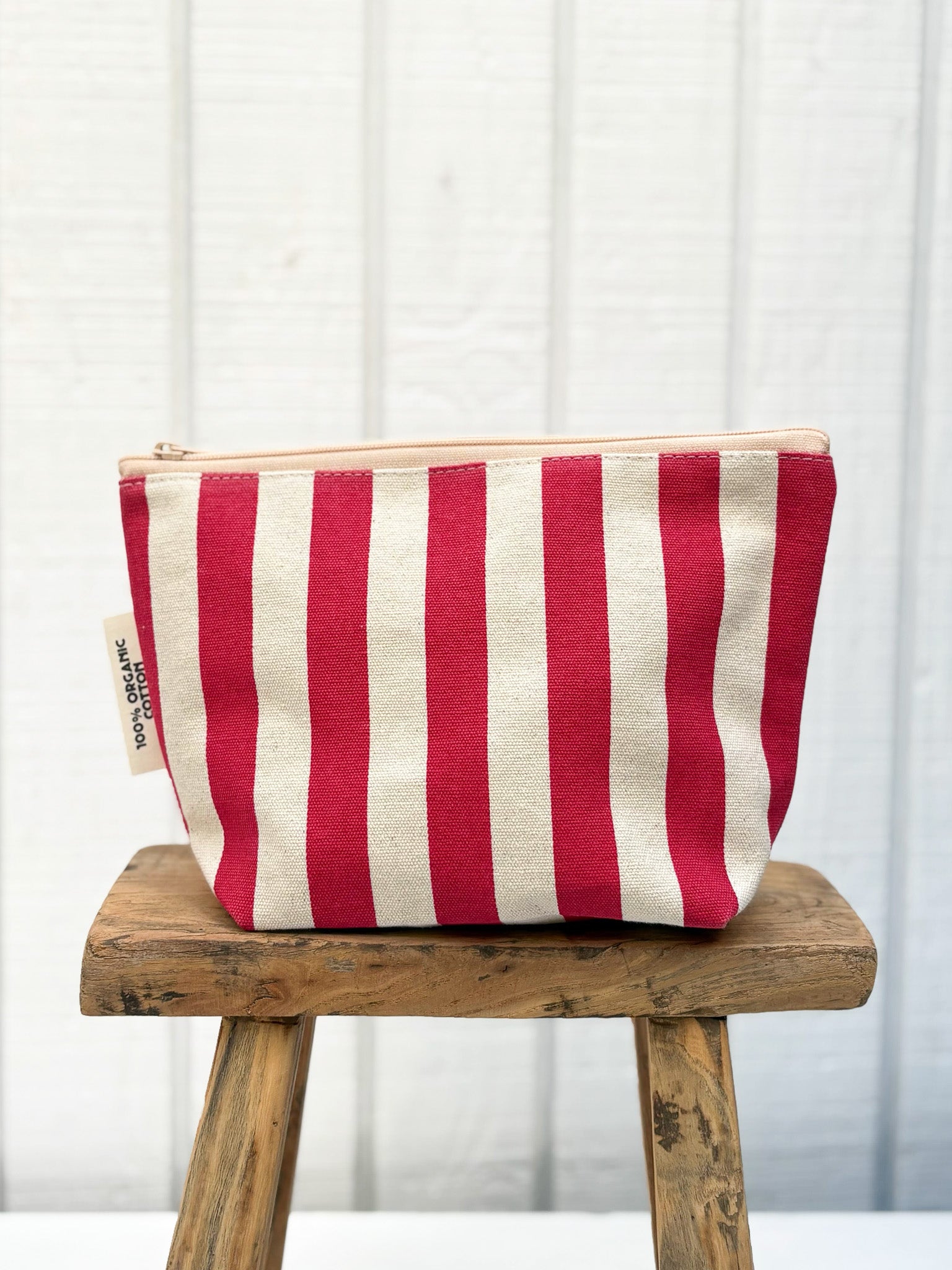 Red and white striped pouch on a wooden stool against a white curtain background