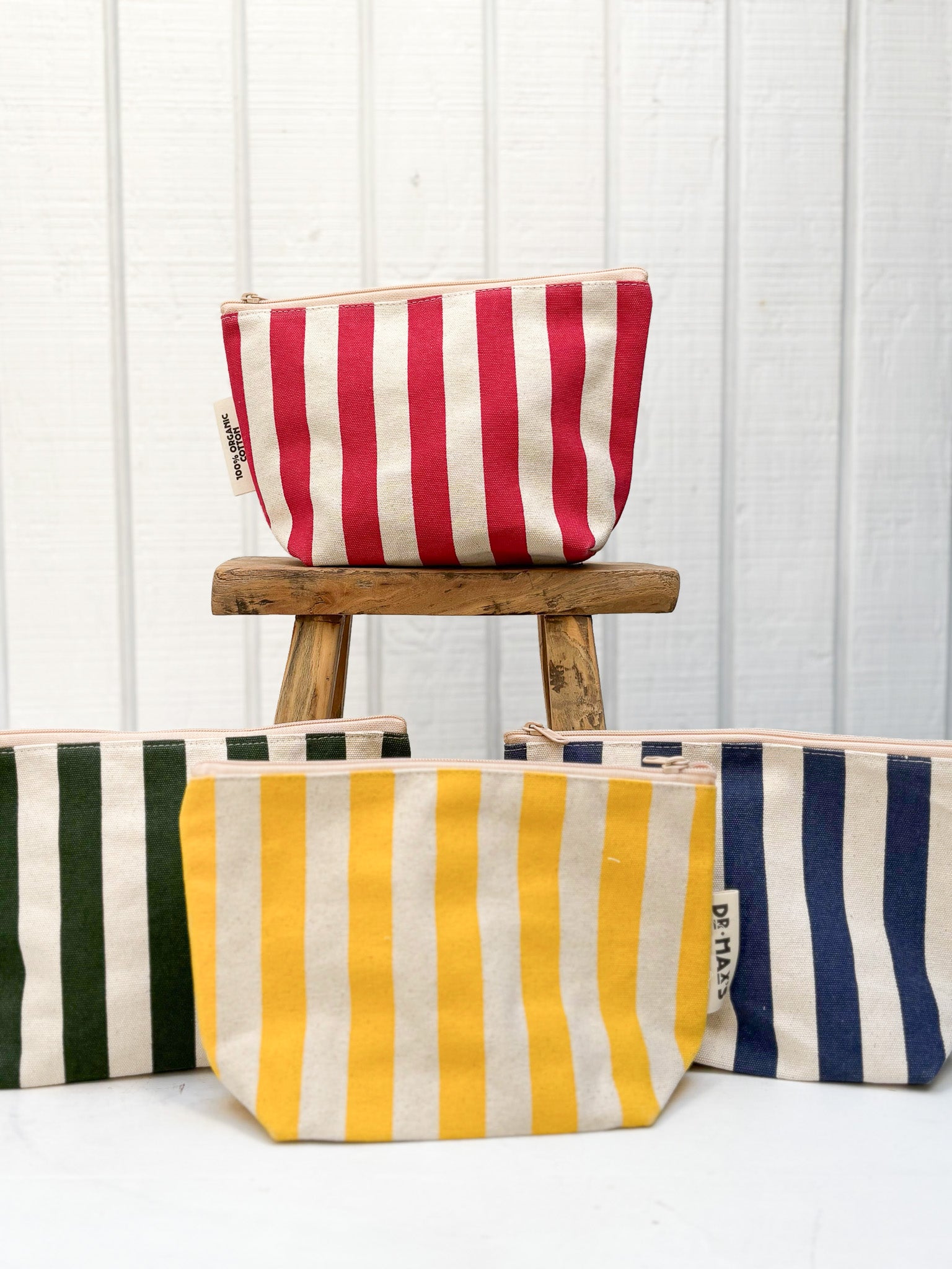 Striped pouches in red, yellow, and blue on a white background with a wooden stool.