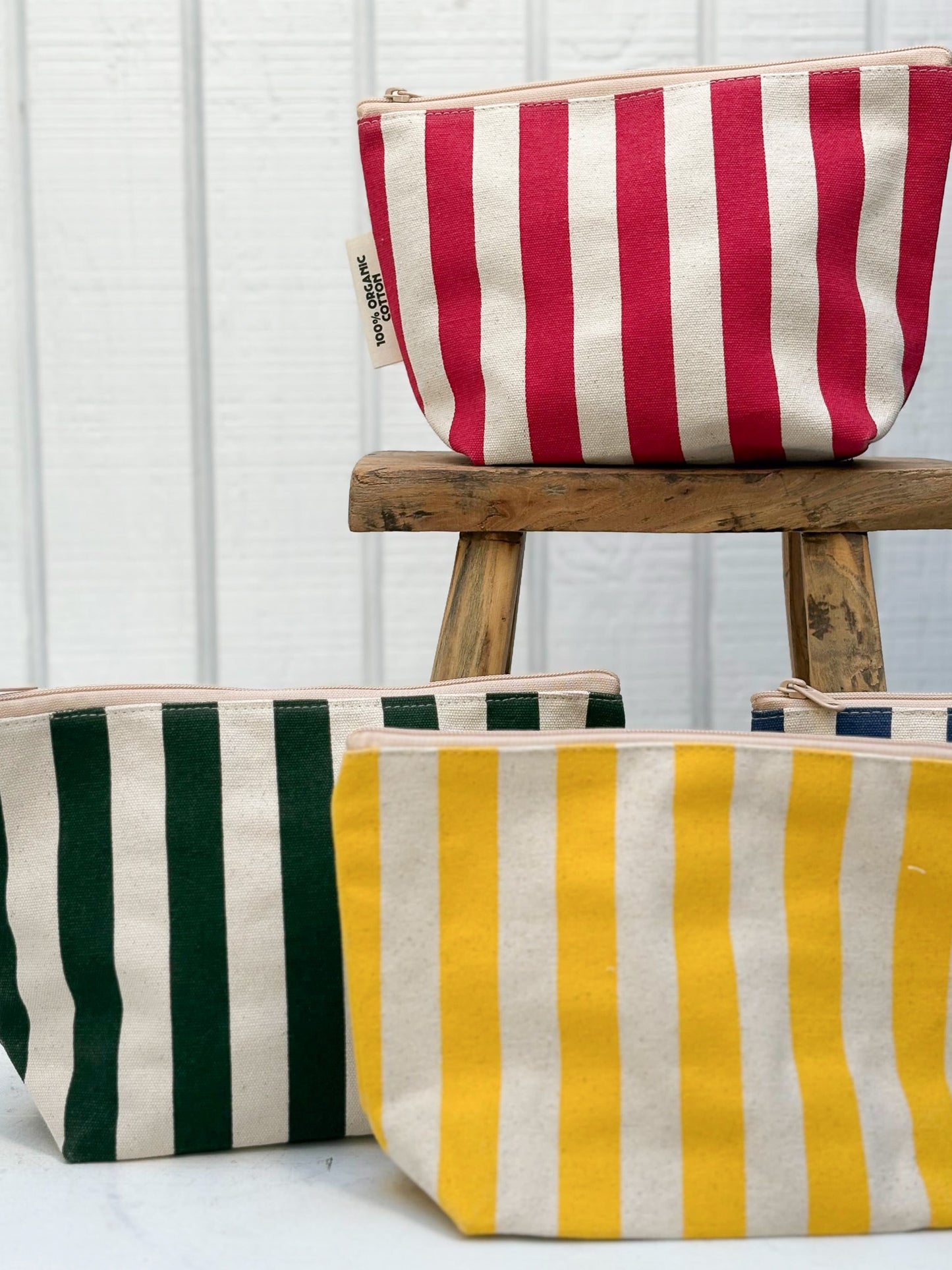 Striped pouches in red, green, and yellow on a wooden stool against a white background