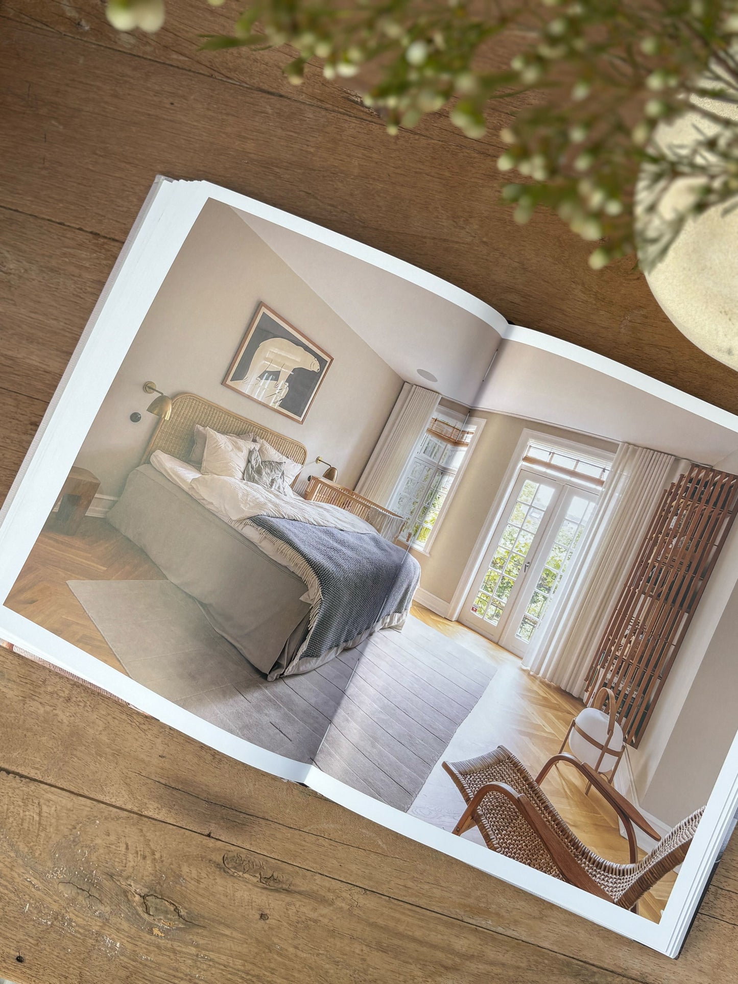 Open photo album showing a bedroom scene on a wooden surface with a plant in the corner.