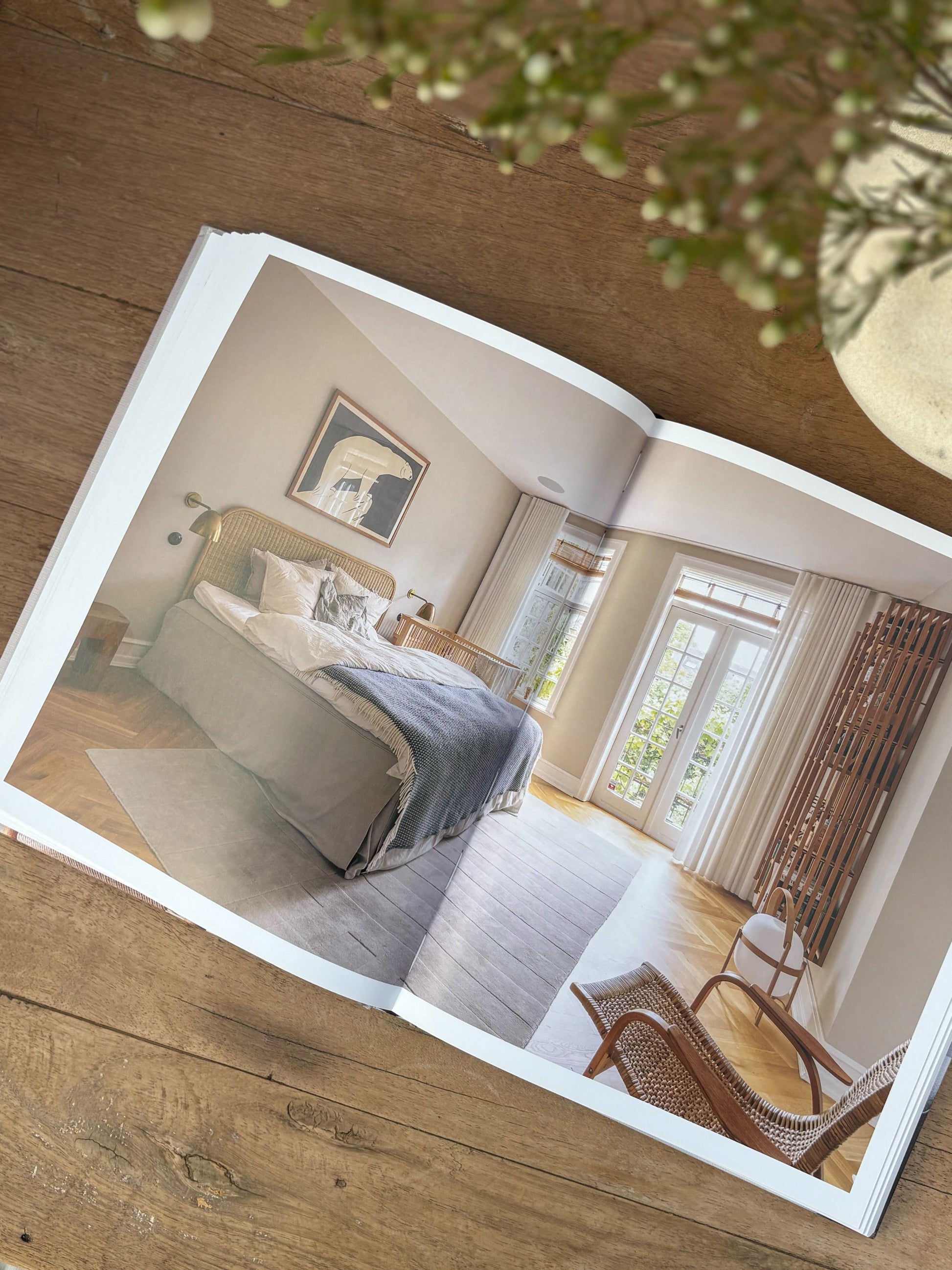 Open photo album showing a bedroom scene on a wooden surface with a plant in the corner.