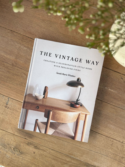 Book titled 'The Vintage Way' on a wooden surface with a blurred plant in the background
