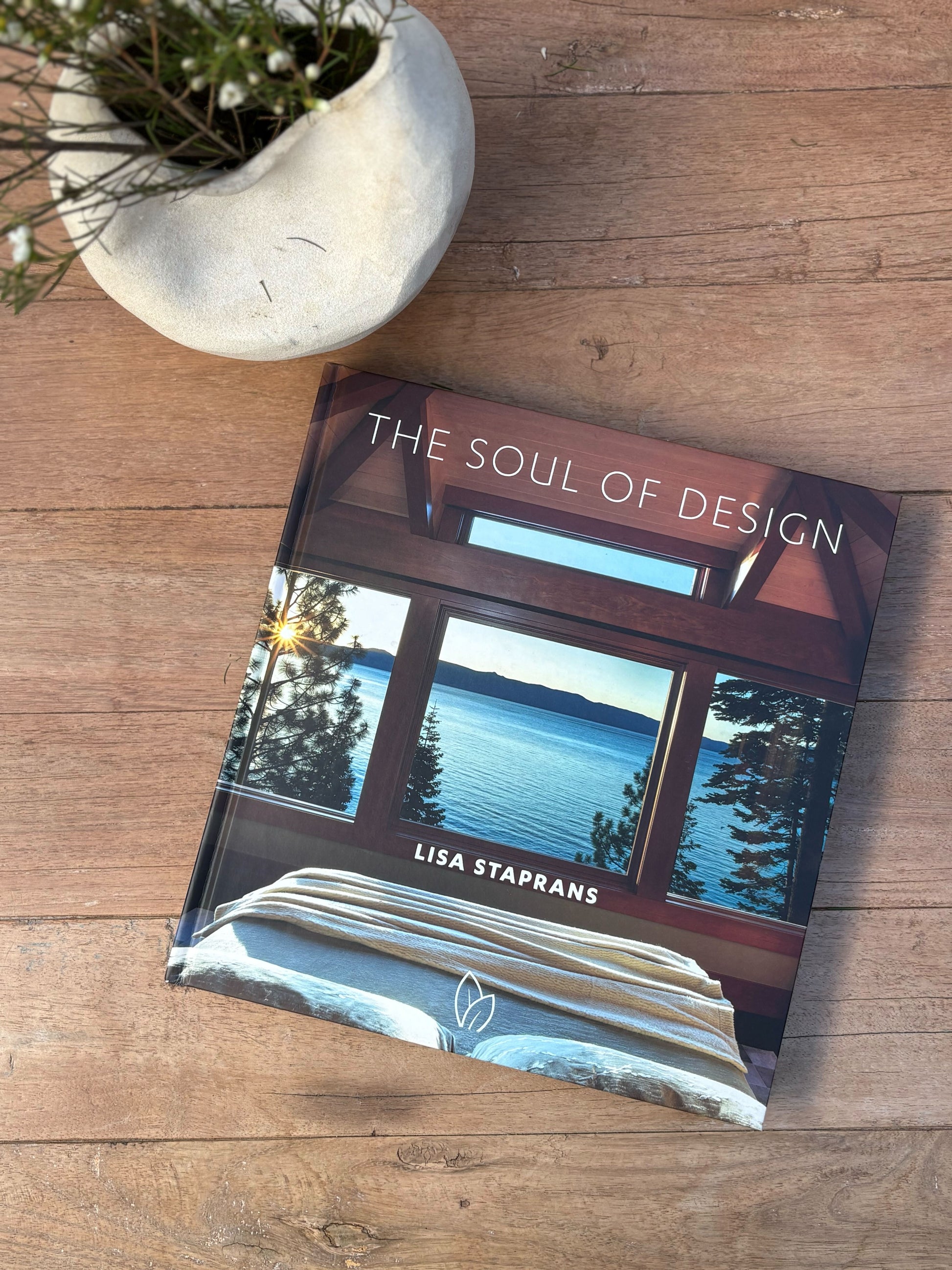 Book titled 'The Soul of Design' by Lisa Staprans on a wooden surface with a plant pot.