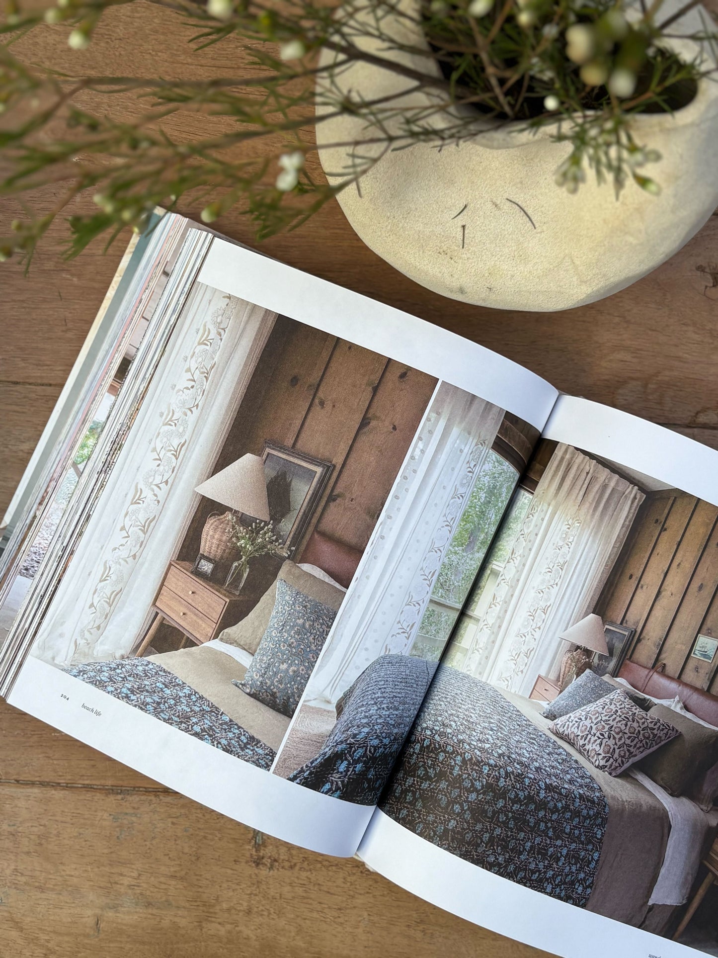 Open book showing interior design images on a wooden surface with a plant.