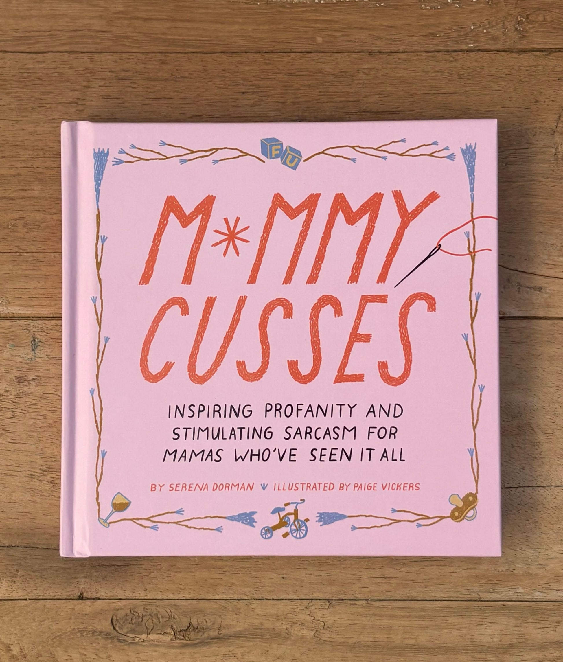 Book titled 'M*mmy Cusses' on a wooden surface