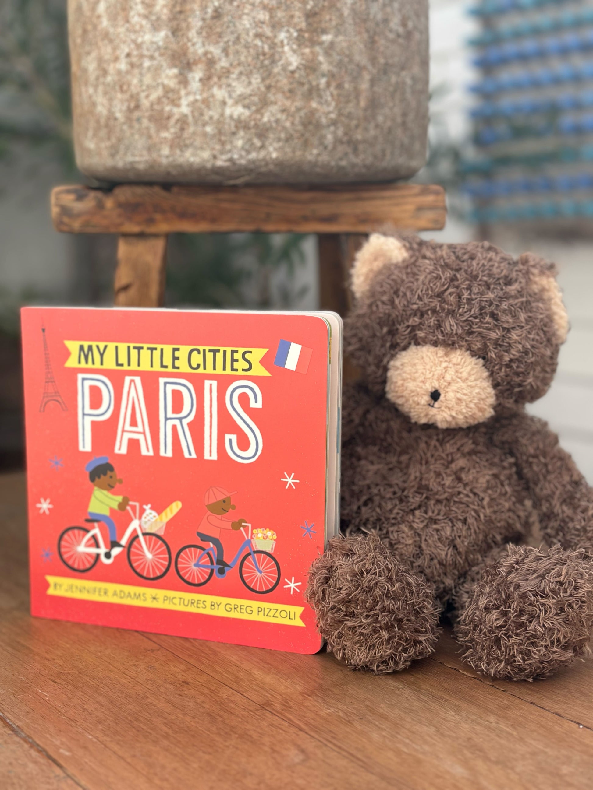 Children's book titled 'My Little Cities: Paris' next to a plush teddy bear on a wooden surface.