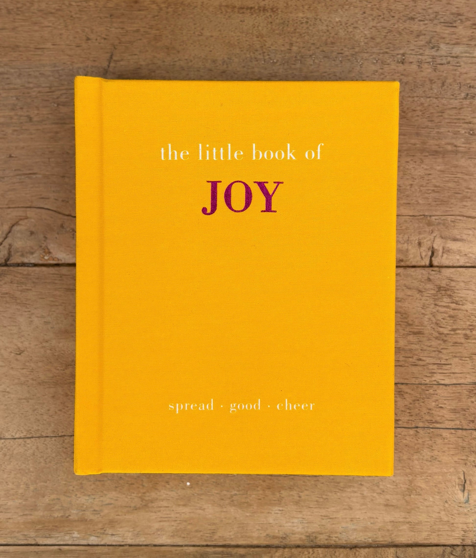 Yellow book titled 'the little book of JOY' on a wooden surface