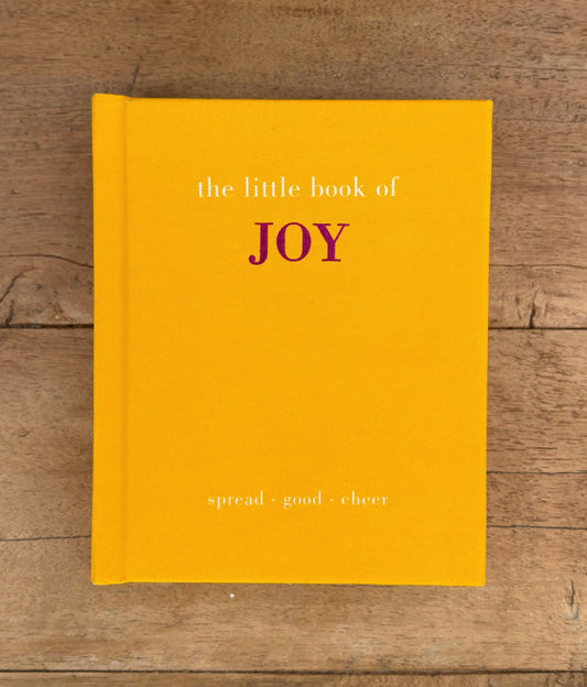 Yellow book titled 'the little book of JOY' on a wooden surface