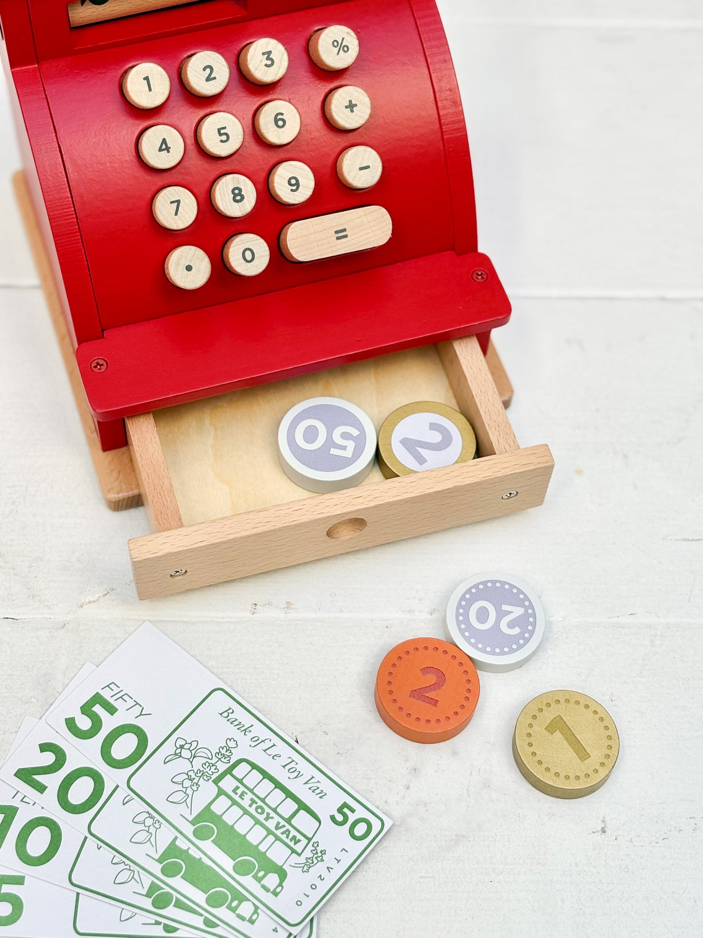 Wooden toy cash register with buttons and coins on a white surface