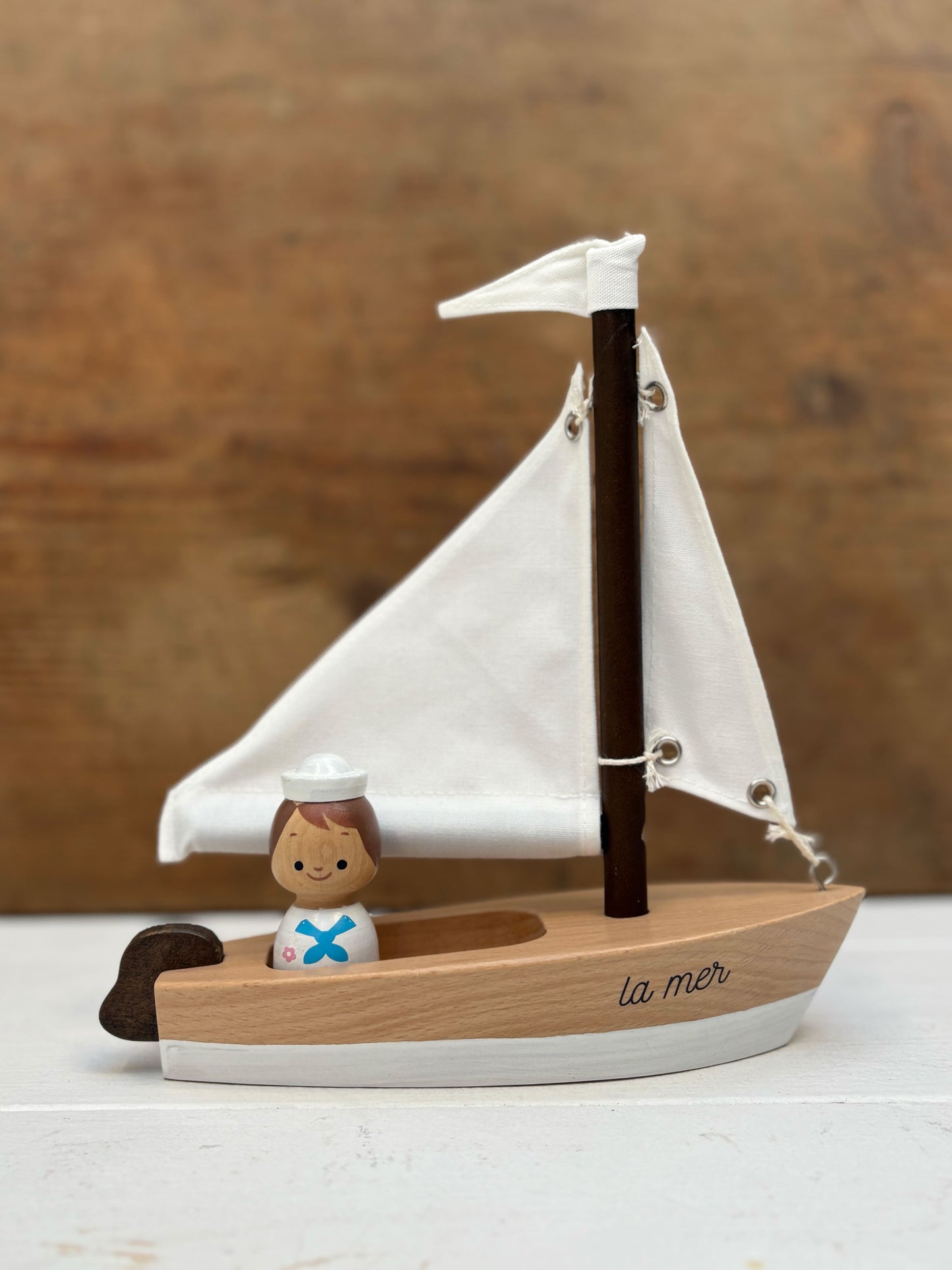 Wooden toy sailboat with a small figure of a sailor on a wooden background