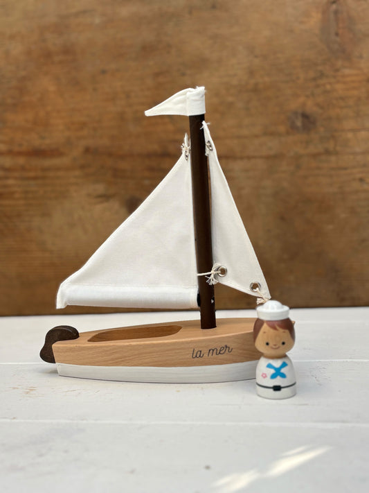 Wooden sailboat model with a small figure on a wooden surface