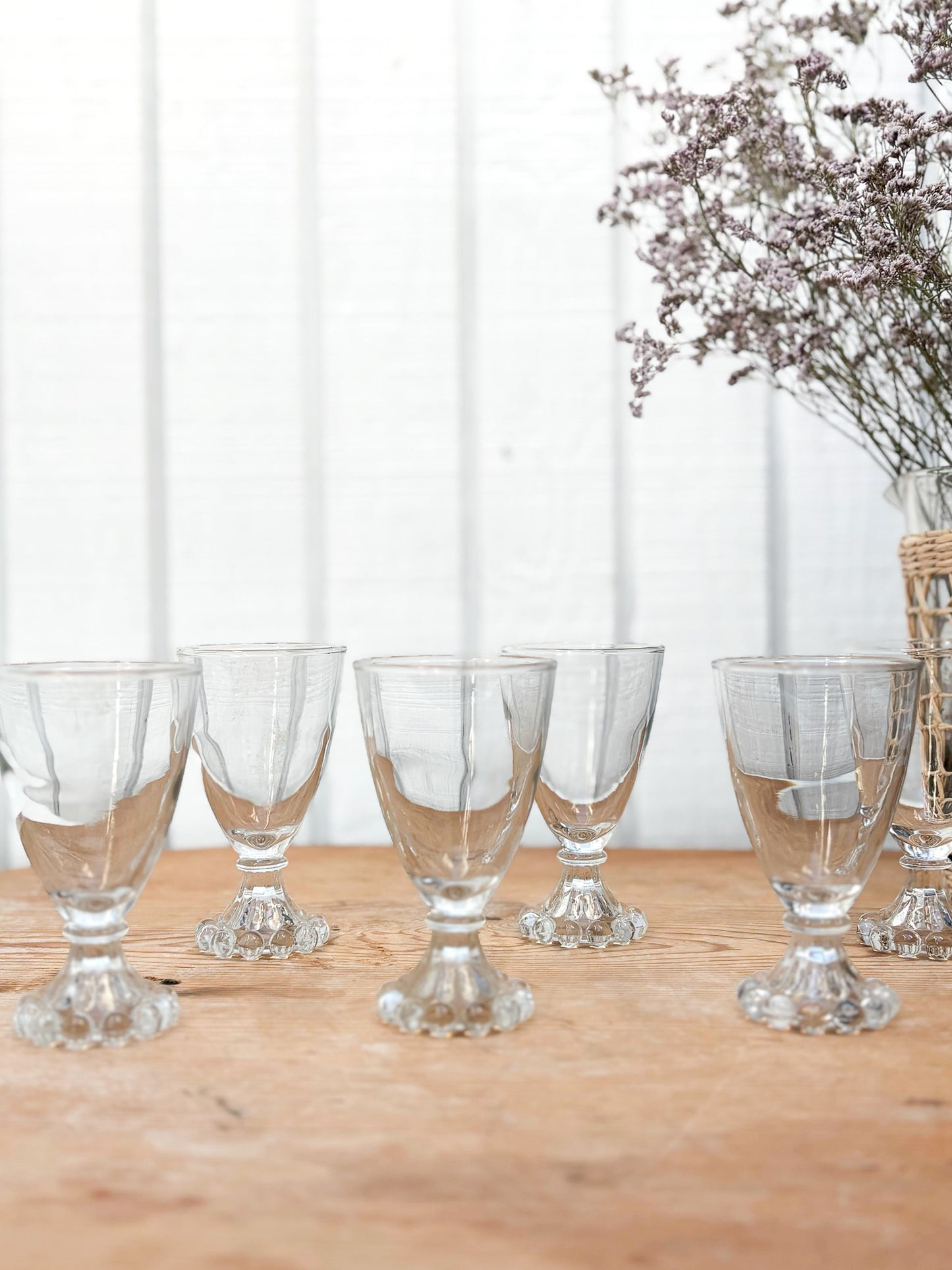 Set of clear glass goblets on a wooden table with a white curtain background