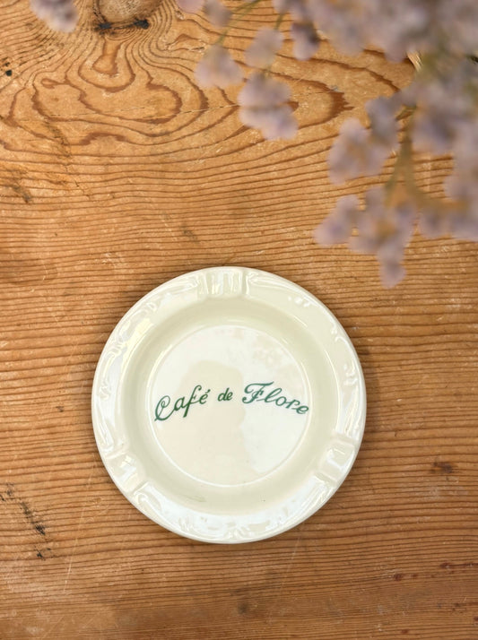 White ceramic plate with 'Café de Flore' text on a wooden surface with flowers.