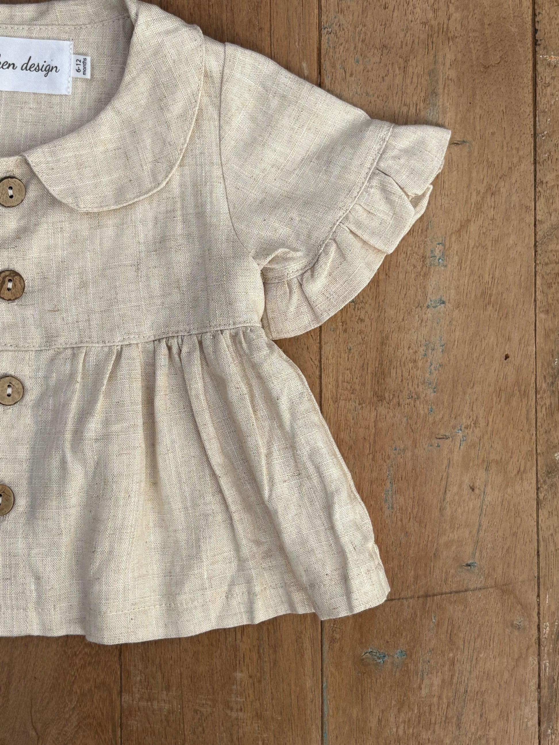 Beige baby dress with ruffled sleeves on a wooden surface