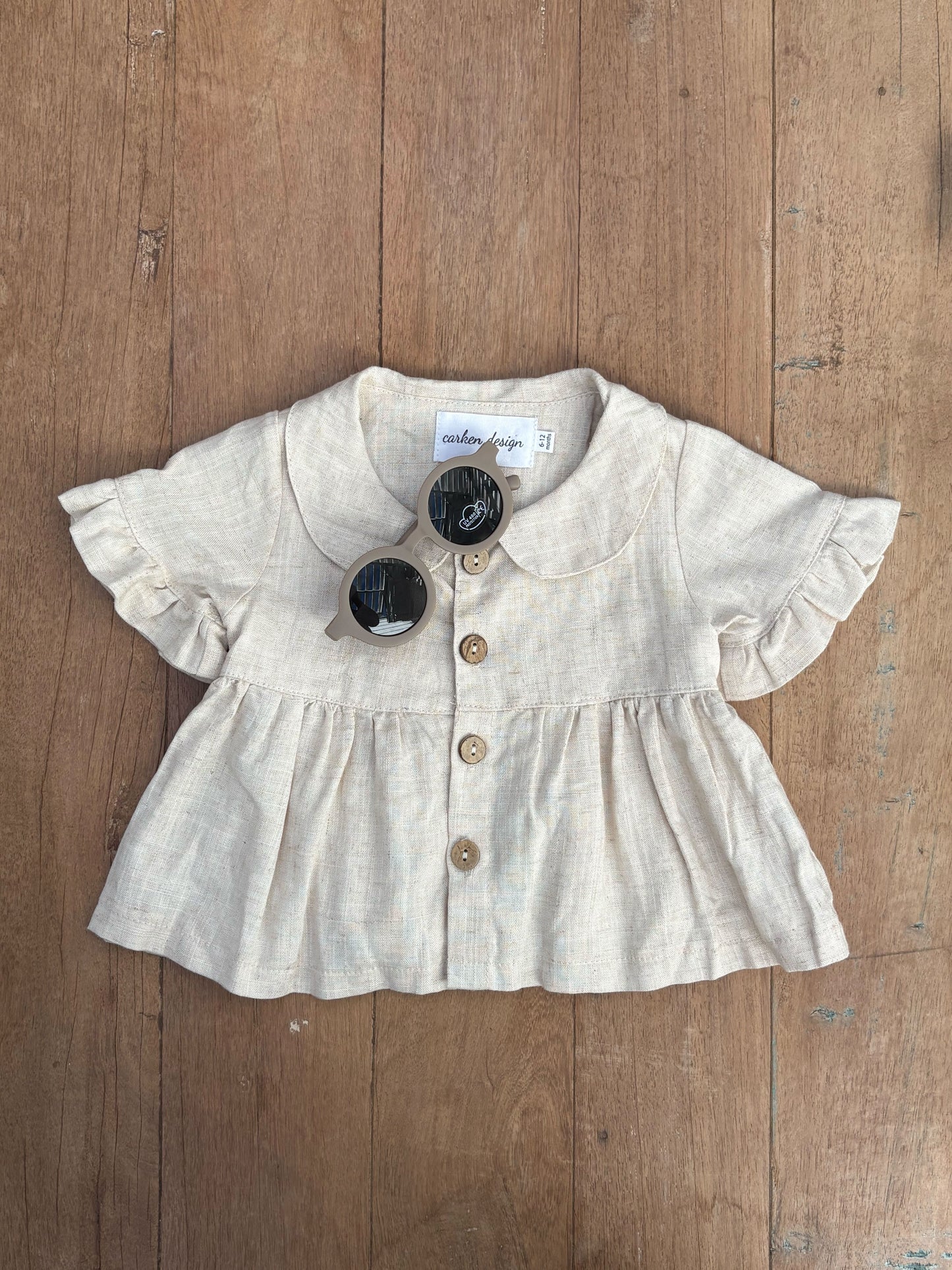 Baby girl's beige blouse with ruffled sleeves and buttons on a wooden surface
