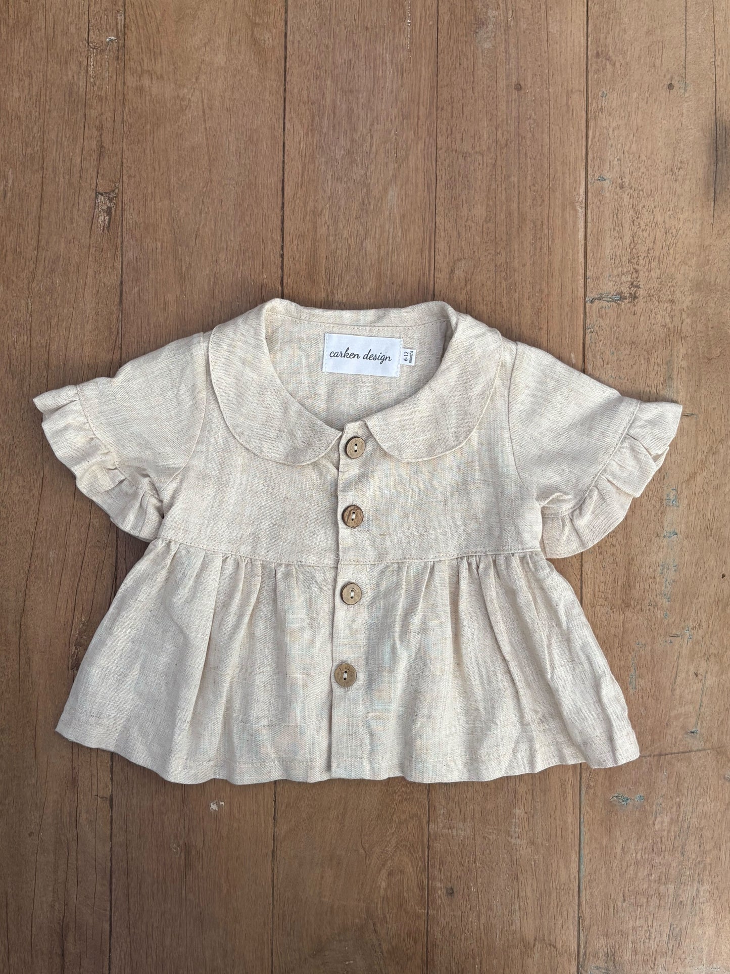 Baby blouse with ruffled sleeves and buttons on a wooden surface
