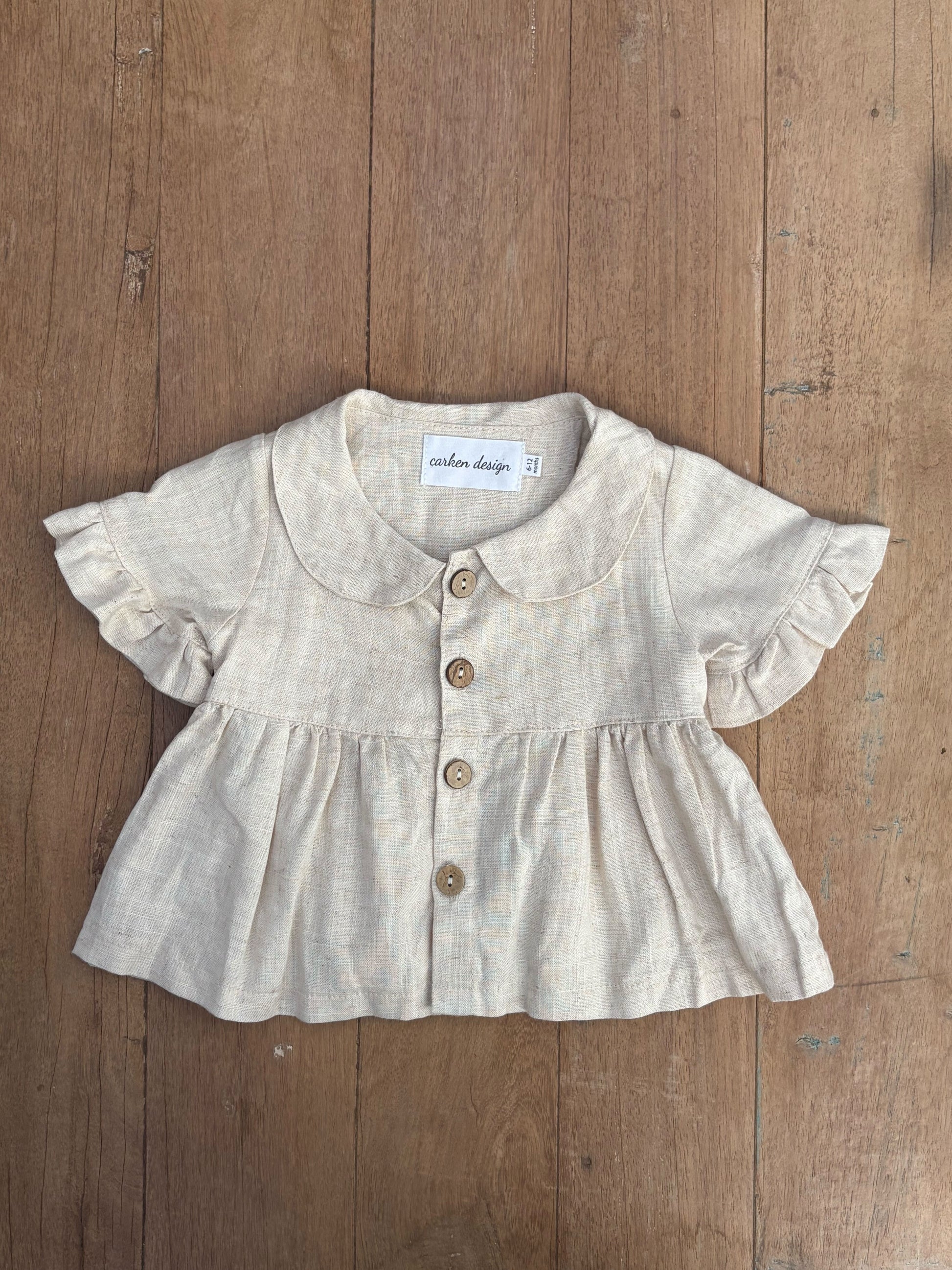 Baby blouse with ruffled sleeves and buttons on a wooden surface