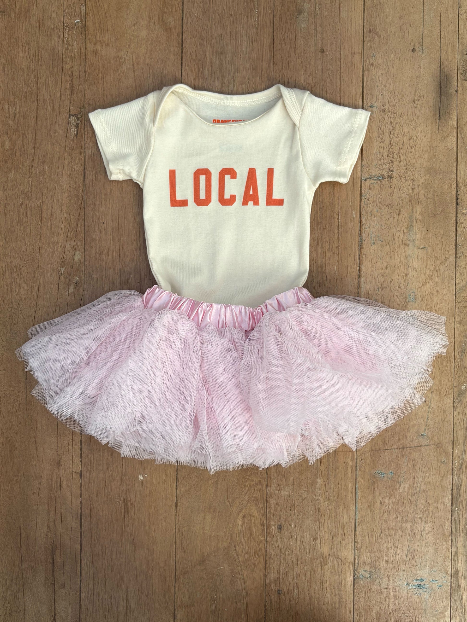 Baby onesie with pink tutu on a wooden surface