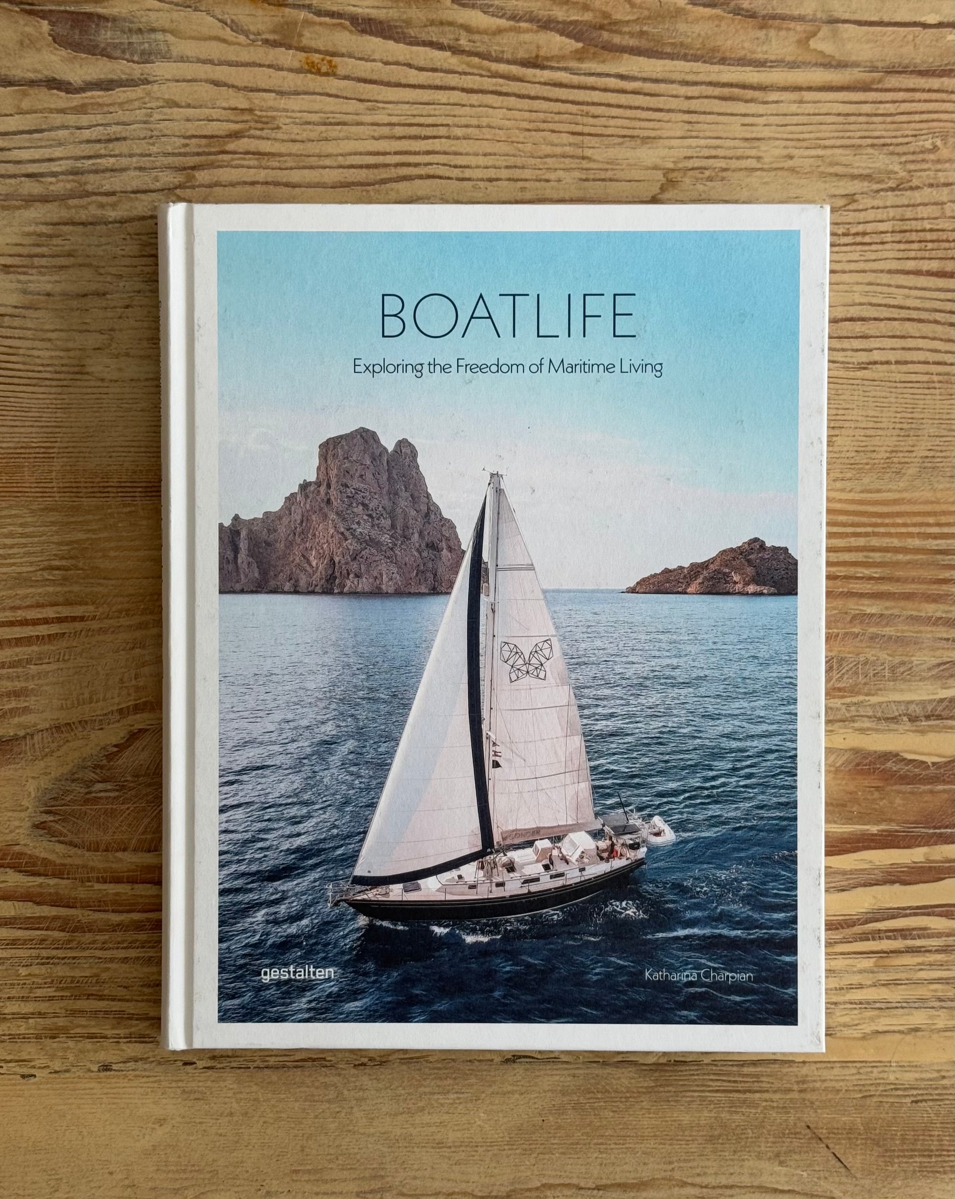Book titled 'BOATLIFE' on a wooden surface with a sailboat and mountain background.