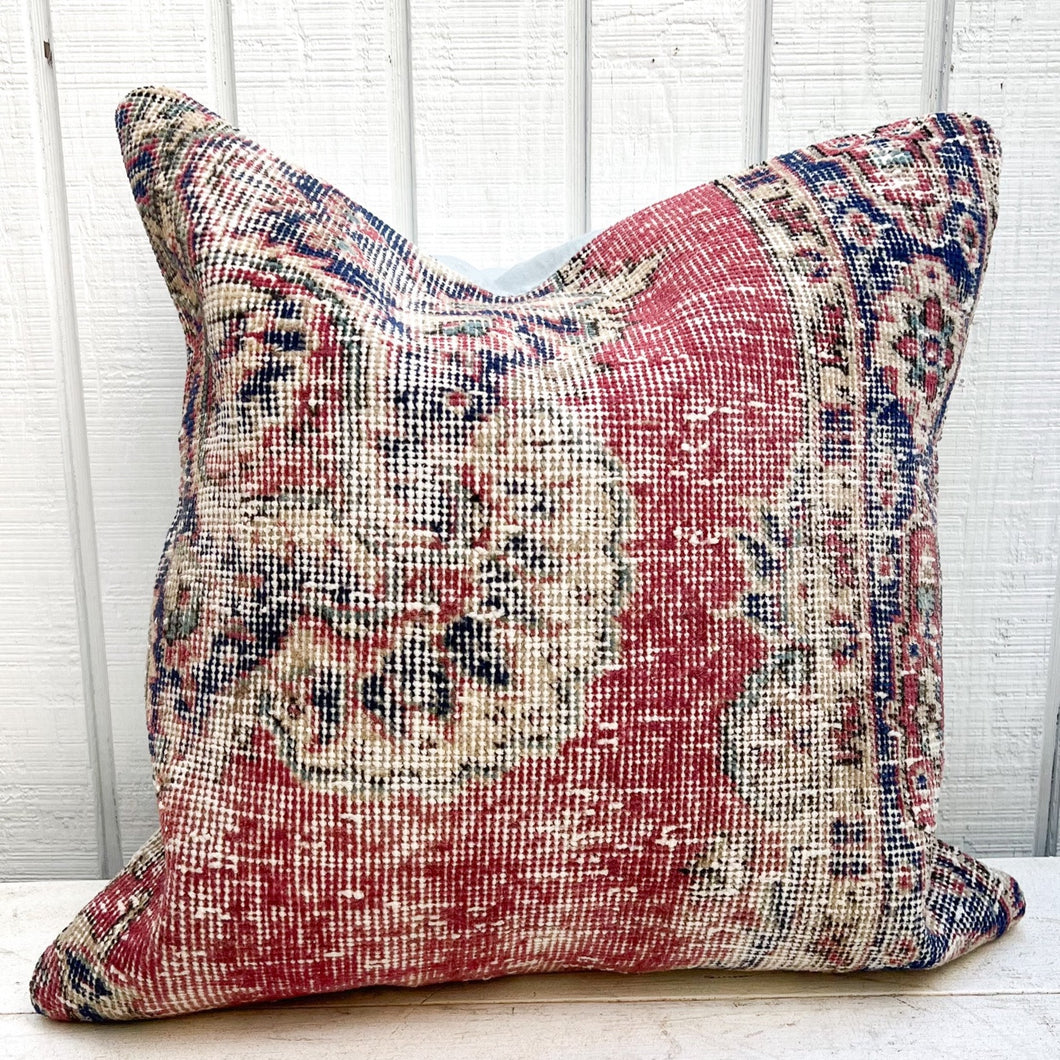 square pillow made from Turkish rug fabric with reds, navy blues and cream colors