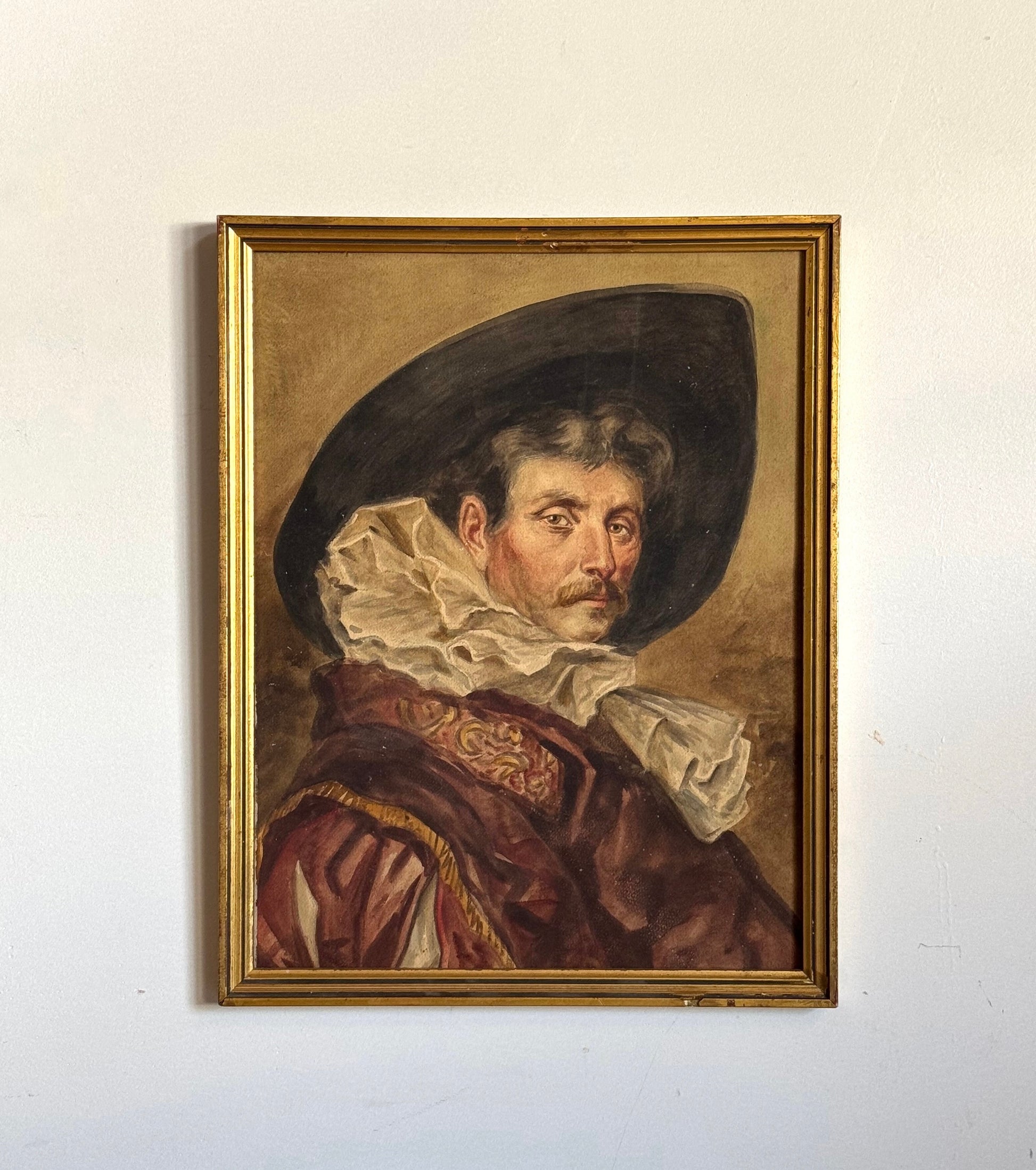 Framed portrait painting of a man with a wide-brimmed hat on a white wall.