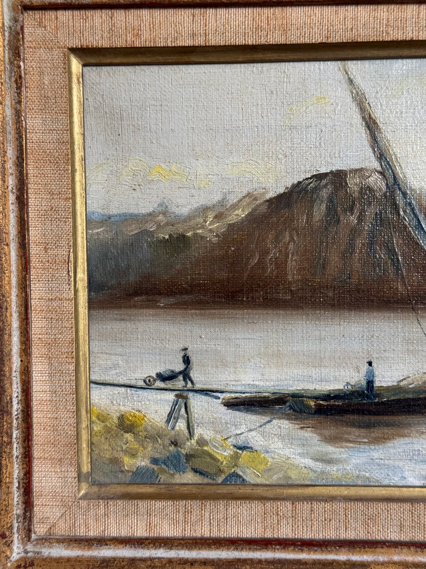 Small painting of a landscape with mountains and people by a lake, framed in gold.