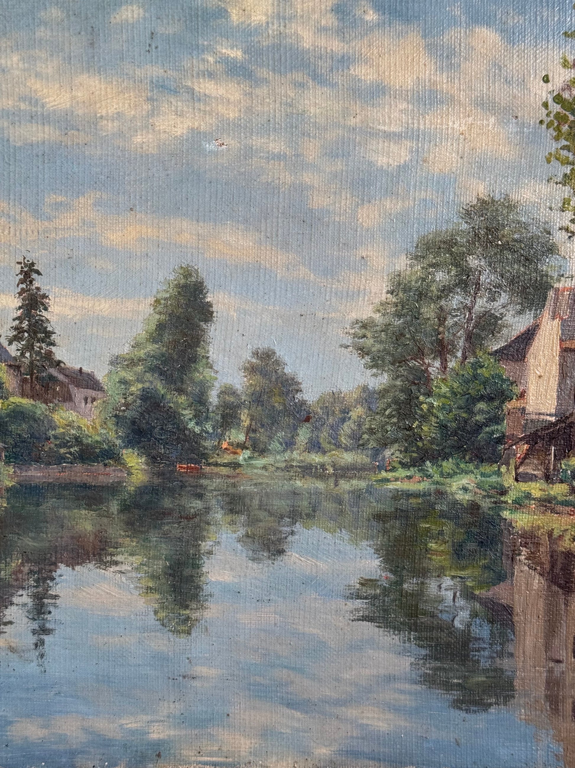 River scene with trees and houses under a blue sky with clouds