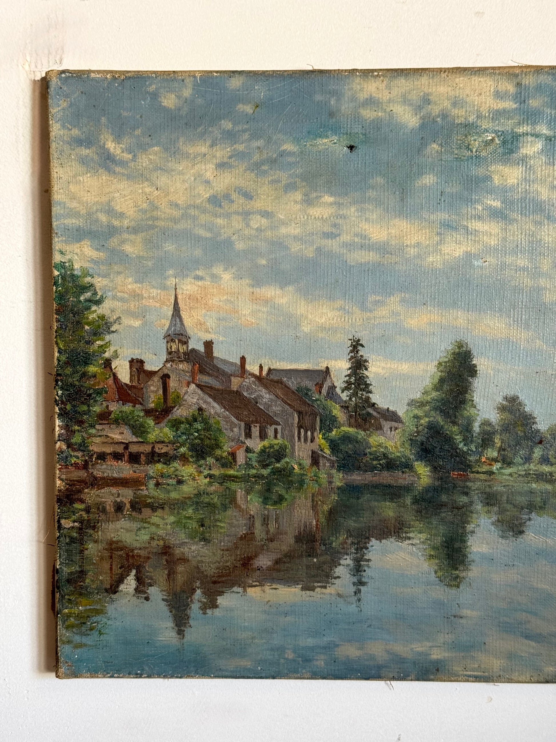 Painting of a village by a lake with trees and a church steeple.